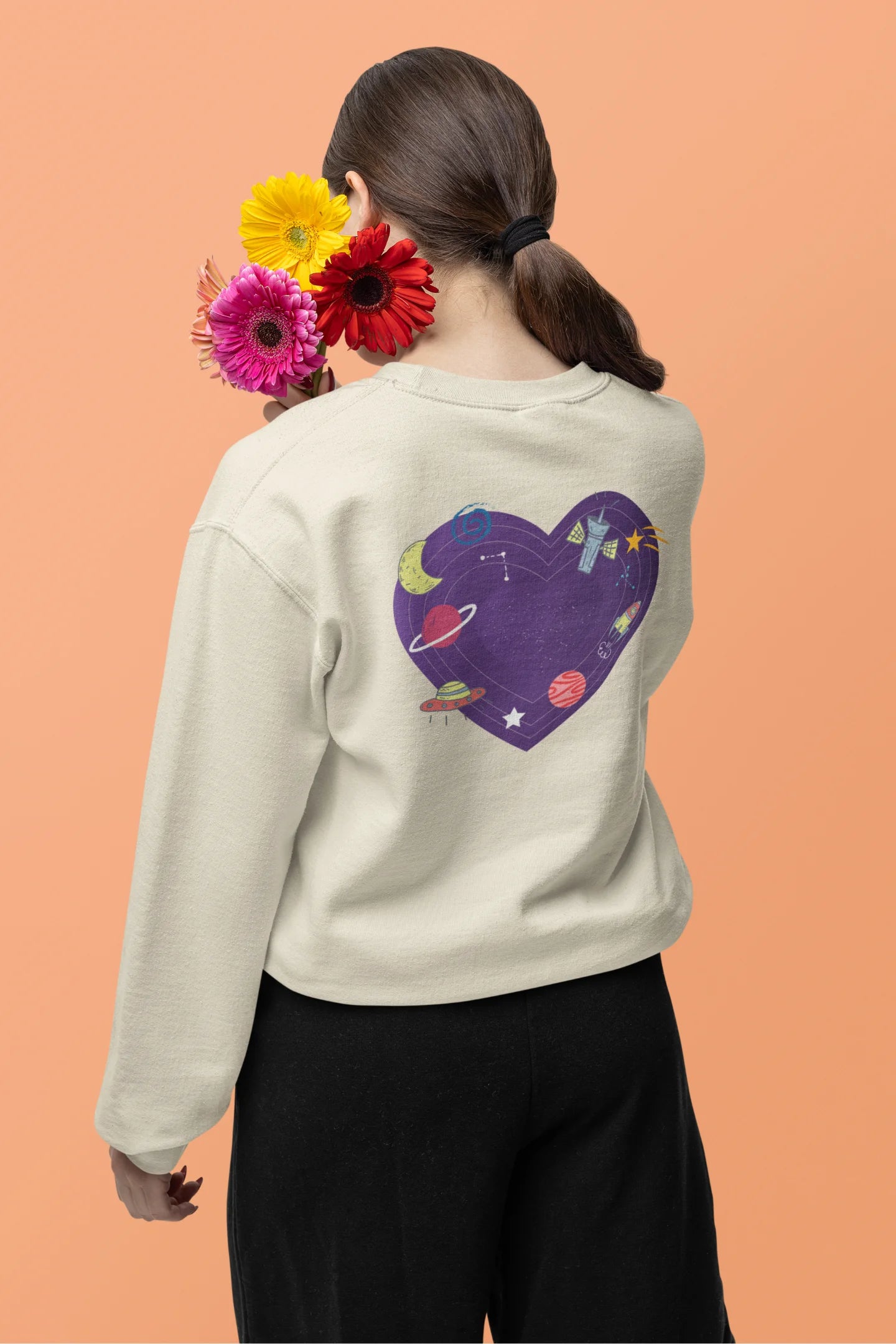 Back view of a female model wearing an cream sweatshirt with the "Paradise" album artwork by Coldplay.
