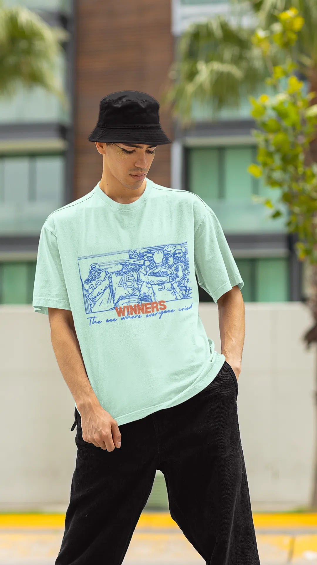 Front view of a male model wearing an mint-green oversized t-shirt featuring a design of the Indian cricket team in a celebratory huddle with the text "Winners" above them. Ideal for Indian cricket fans commemorating their team's World Cup victory.