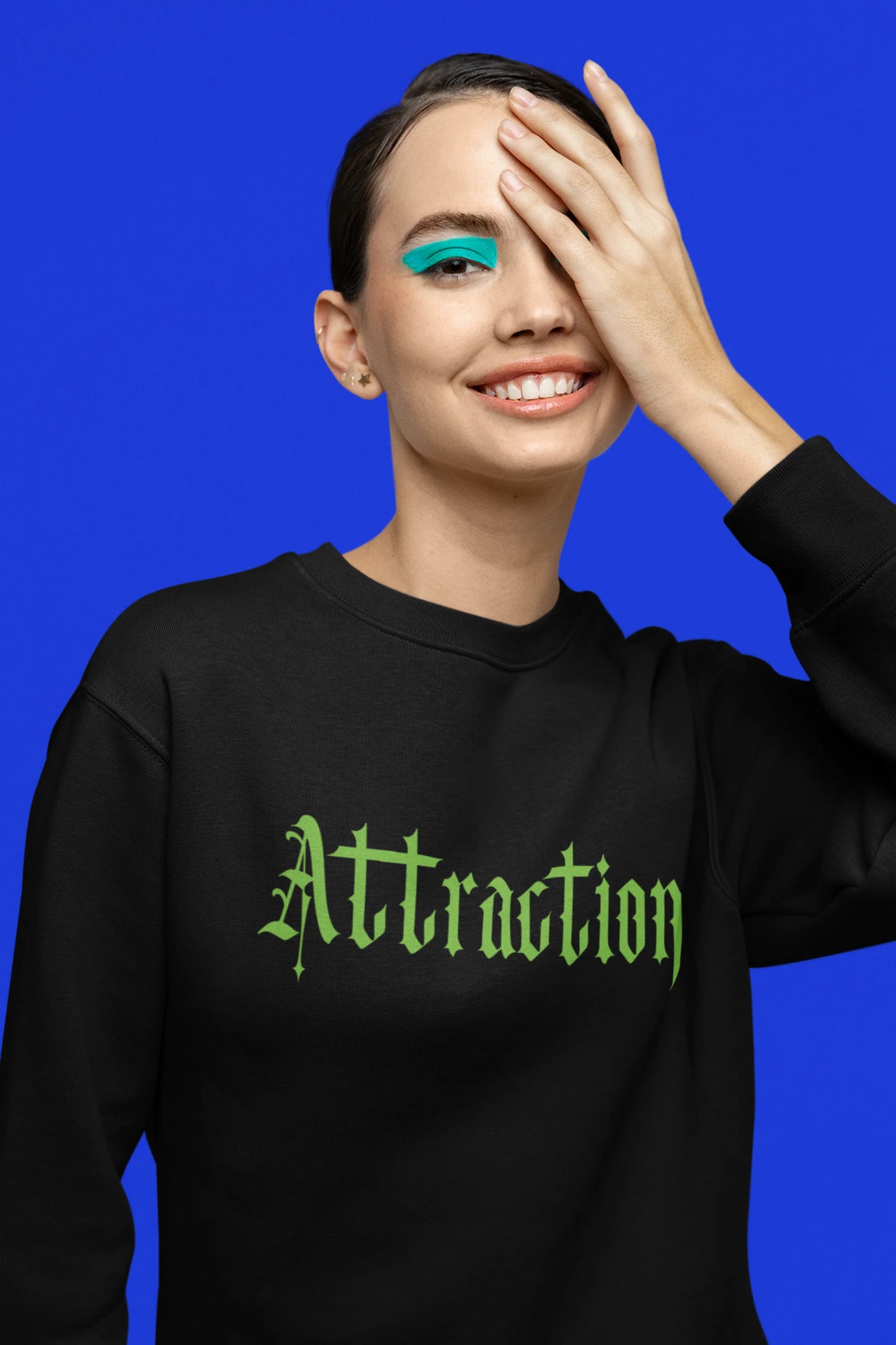 Fourth front view of a female model wearing a black sweatshirt with a brutalist design featuring two statues kissing and the word "Attraction".