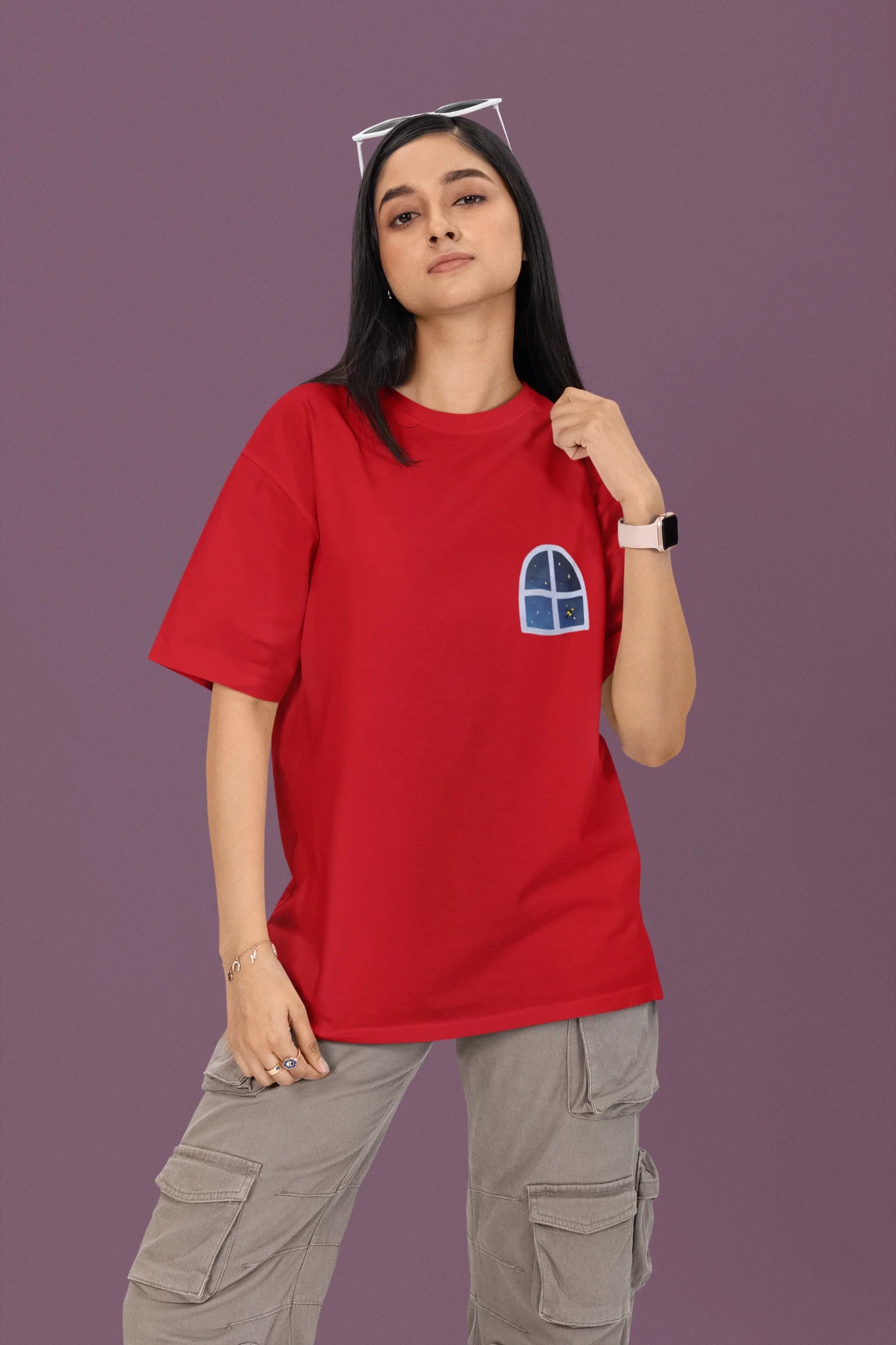 First front view of a female model wearing a red oversized t-shirt featuring an illustration called Mithi Neend of children lying or sitting on a rooftop, looking up at a starry night sky.