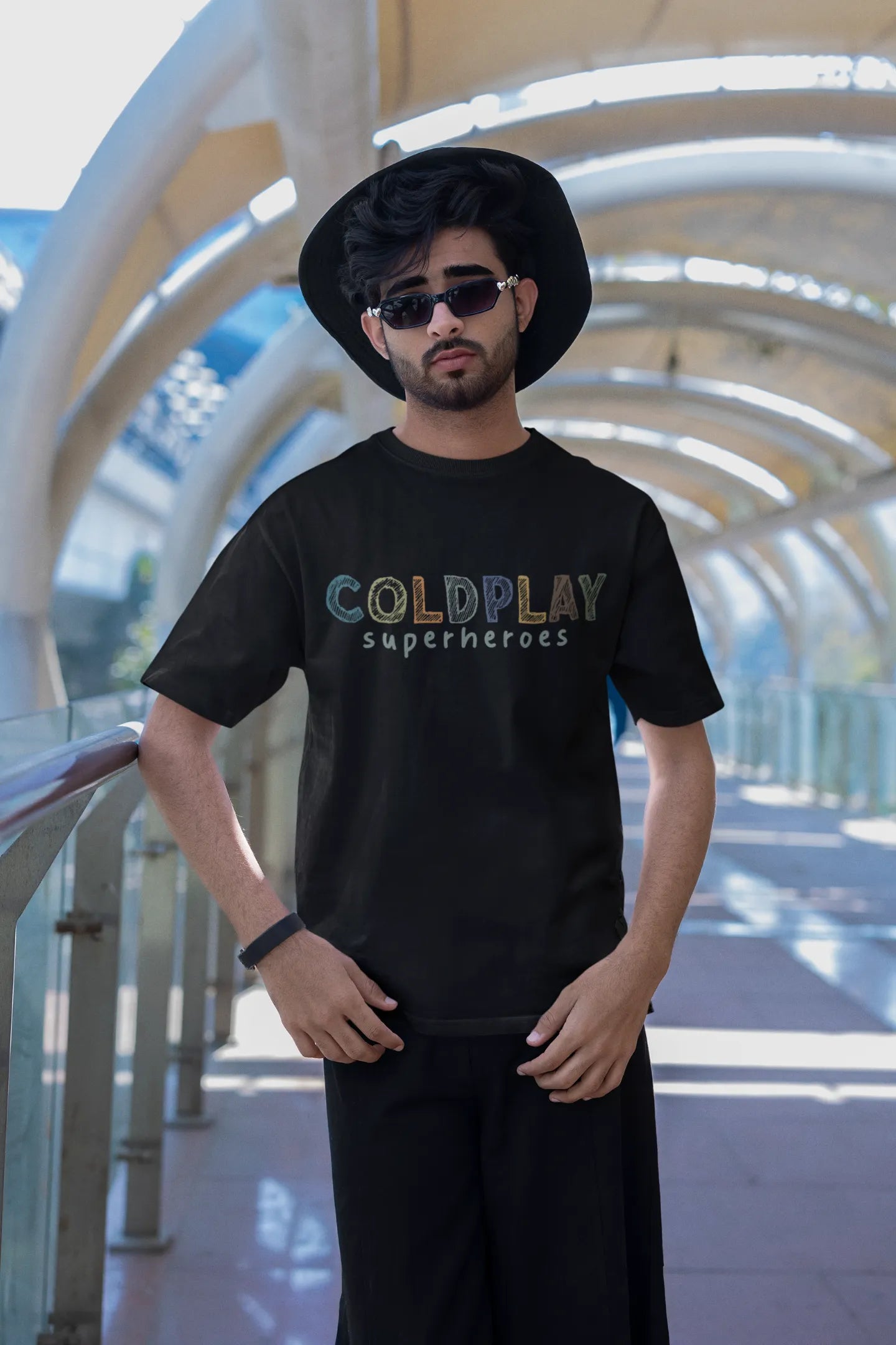 Second view of a male model wearing an black oversized t-shirt with a design inspired by the "Something Just Like This" music video, featuring the word "Superheroes".