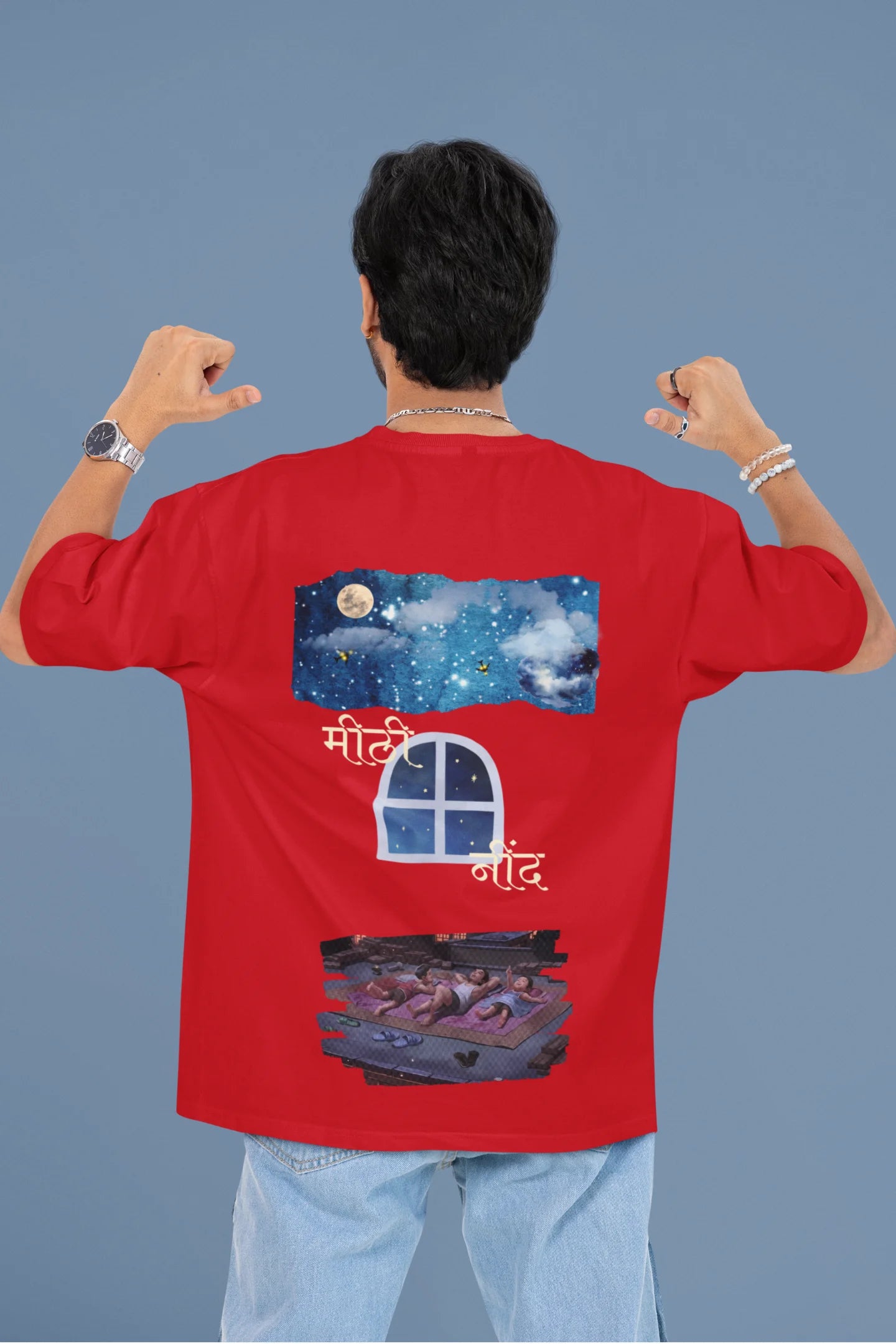 Back view of a male model wearing an oversized t-shirt featuring an illustration called Mithi Neend of children lying or sitting on a rooftop, looking up at a starry night sky.