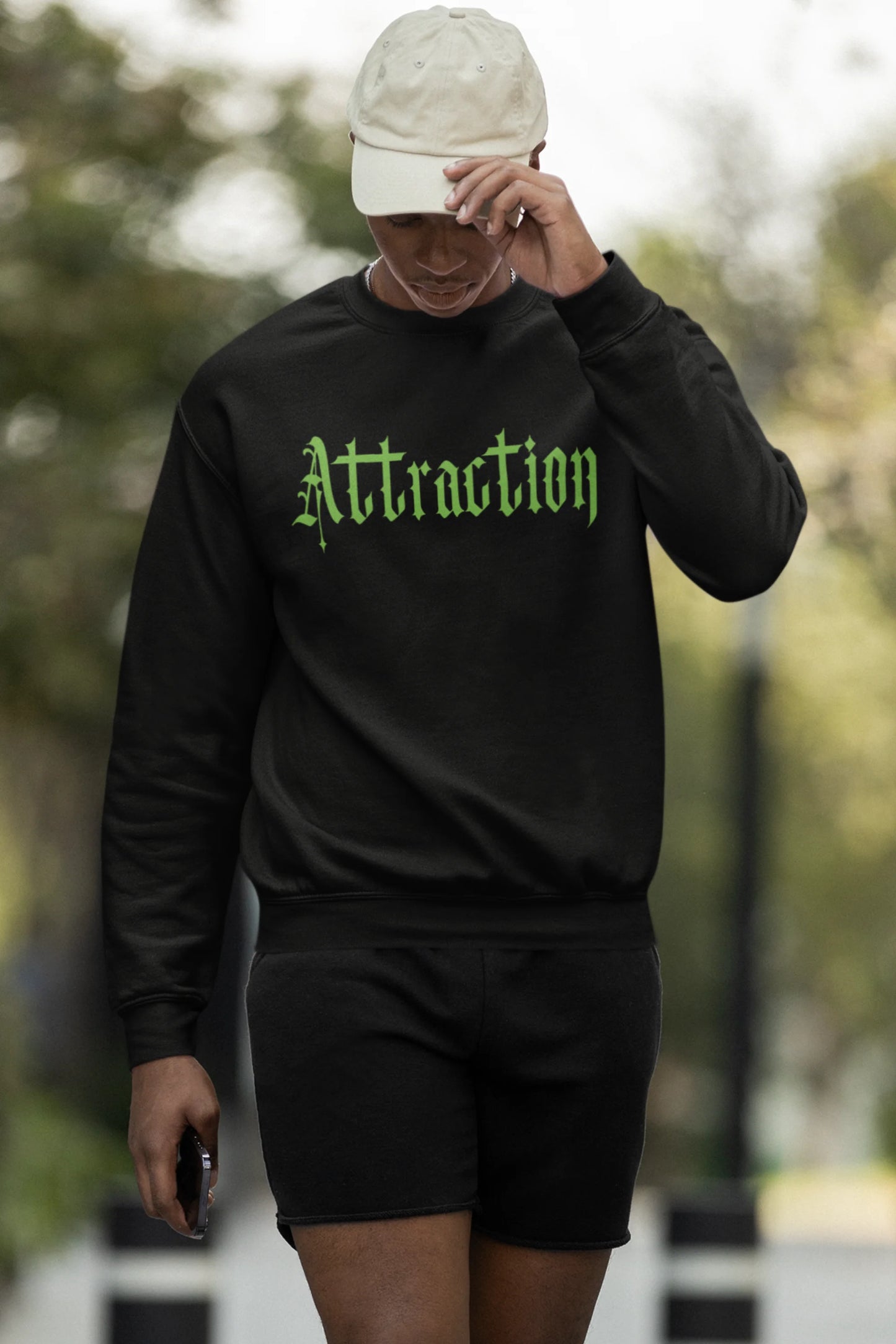 Third front view of a male model wearing a black sweatshirt with a brutalist design featuring two statues kissing and the word "Attraction".