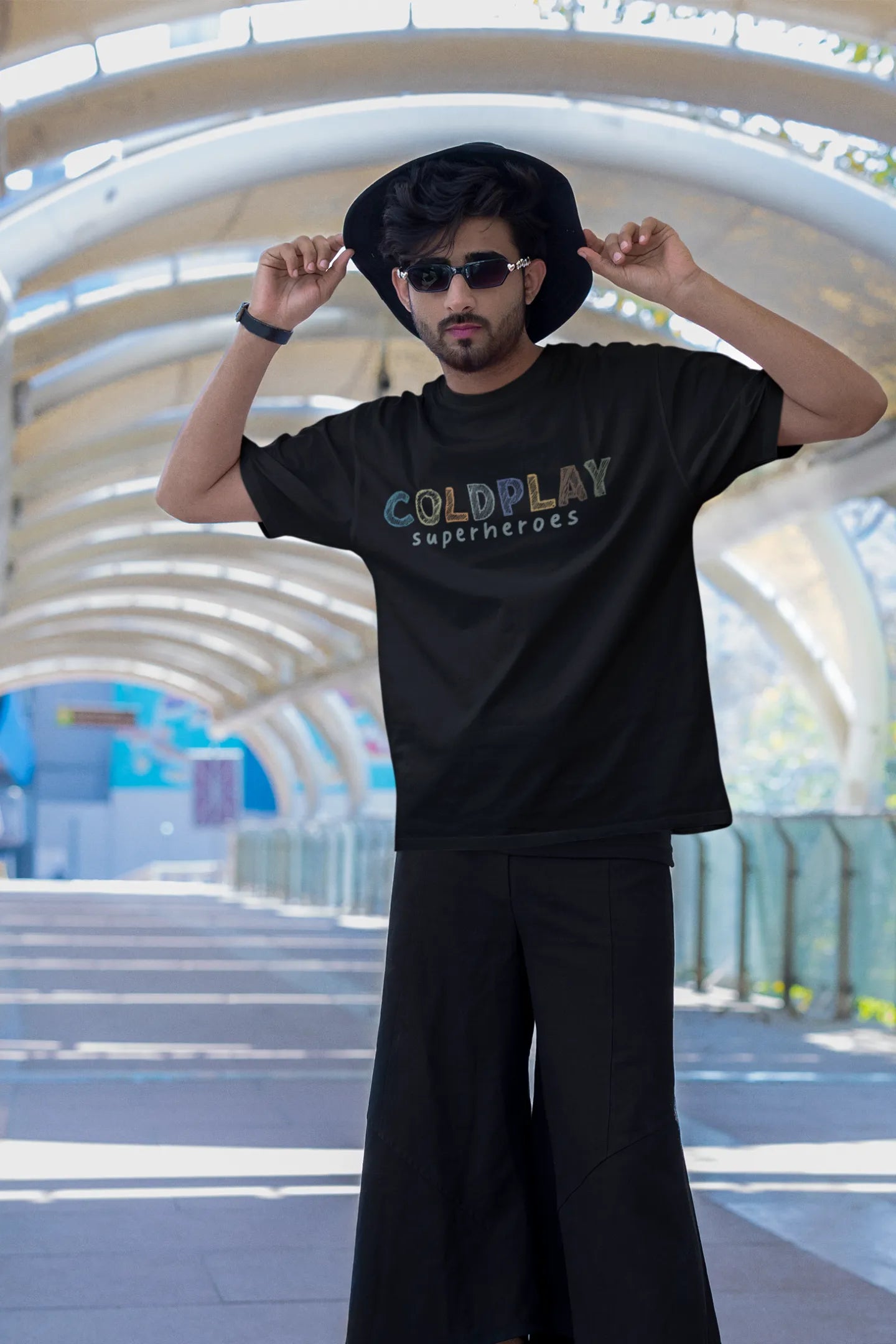 First view of a male model wearing an black oversized t-shirt with a design inspired by the "Something Just Like This" music video, featuring the word "Superheroes".