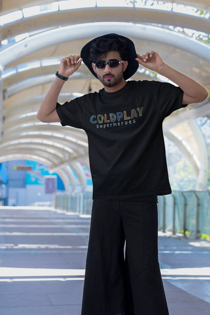 First view of a male model wearing an black oversized t-shirt with a design inspired by the "Something Just Like This" music video, featuring the word "Superheroes".