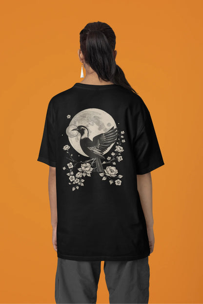Back view of a female model wearing a black oversized tee with a heron taking off under the moonlight.