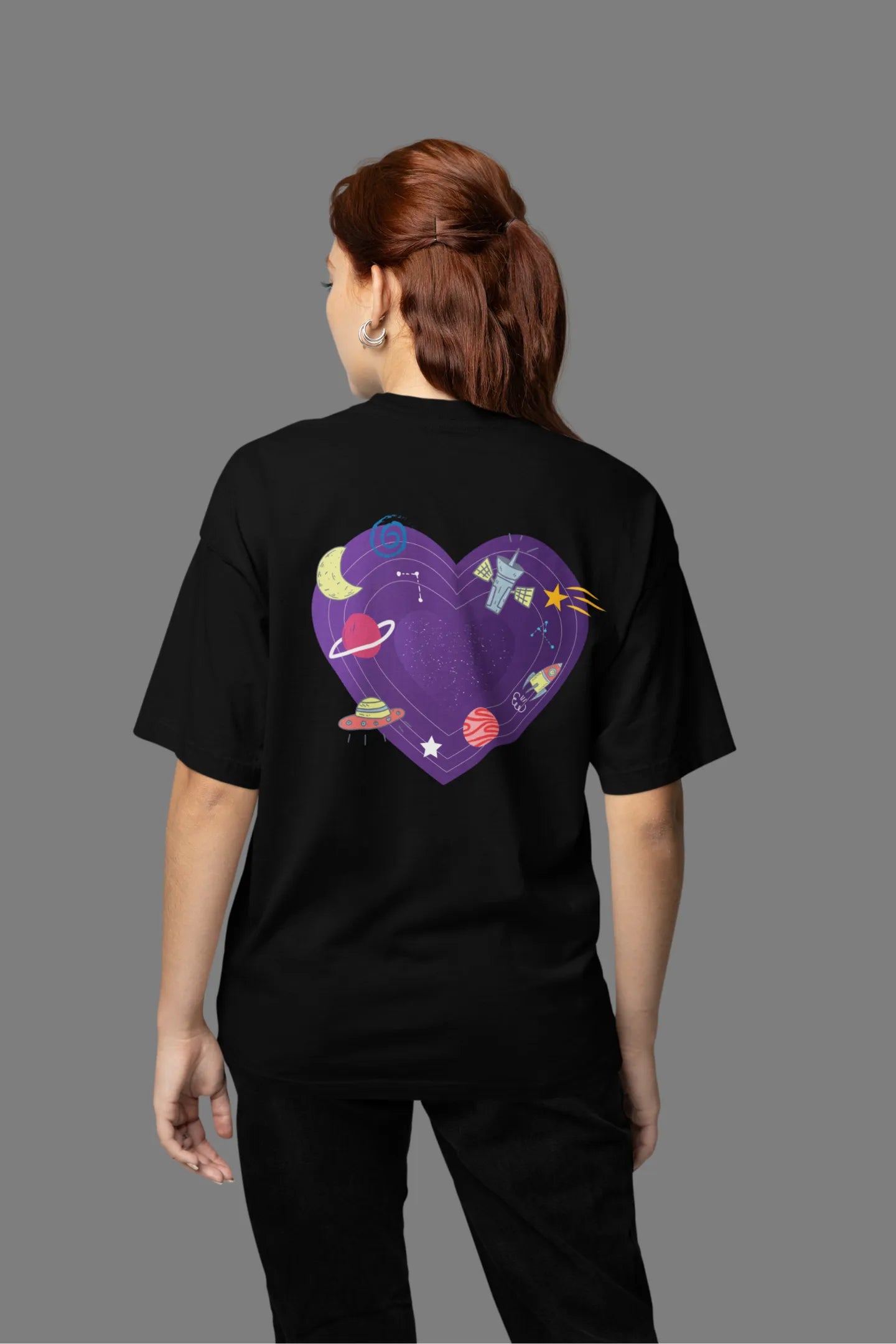 Back view of a female model wearing an black oversized t-shirt with the "Paradise" album artwork by Coldplay.

