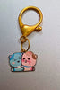 A view of a couples keychain featuring two separate charms depicting cats hugging each other. The cats' colors may vary, including combinations of pink and blue.