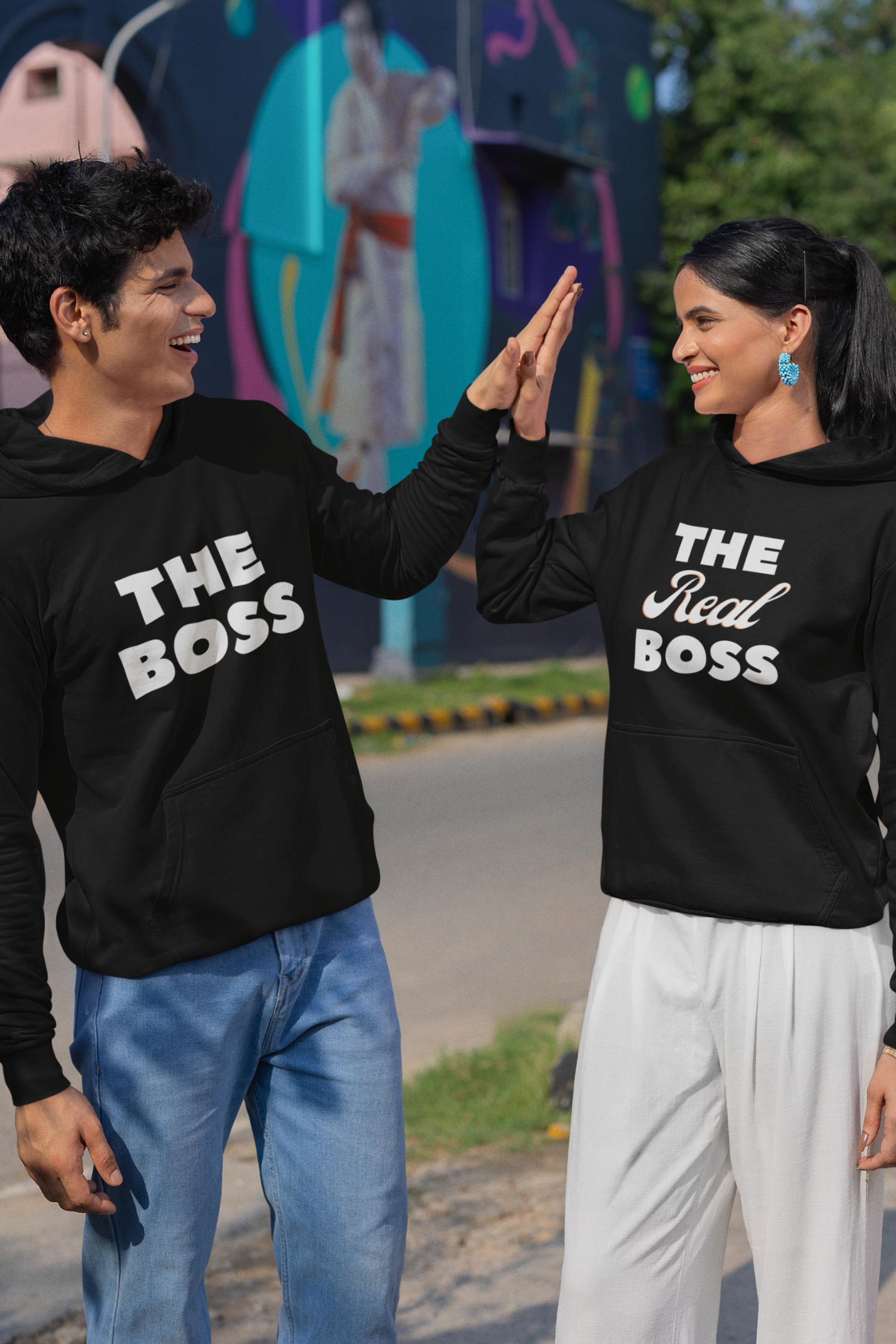 A high fiving couple wearing matching hoodies, one with "The Boss" and the other with "The Real Boss" printed on them.