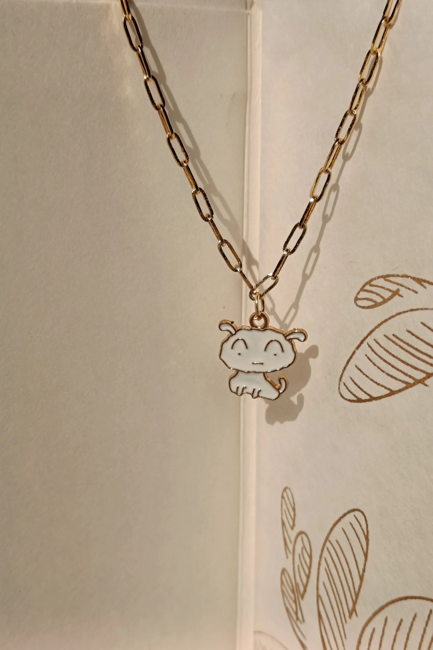 2nd view of a gold chain necklace with a small pendant depicting Shero from the anime Shin Chan.
