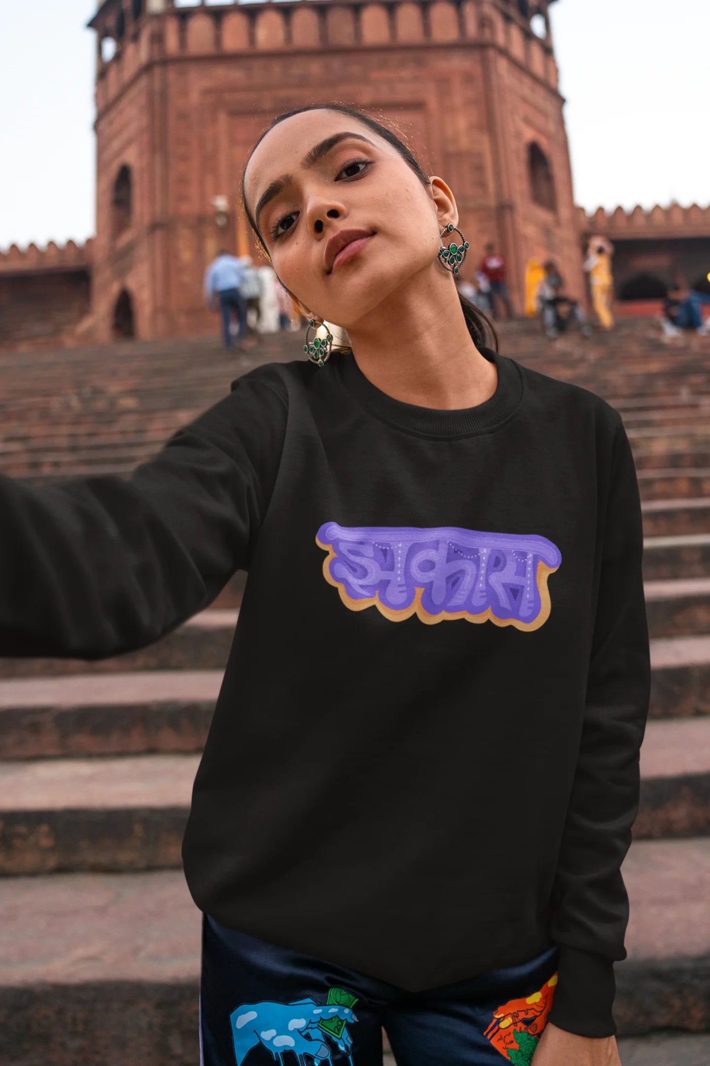 4th front view of a female model wearing an black sweatshirt featuring "Jhakas" in a stylish font.