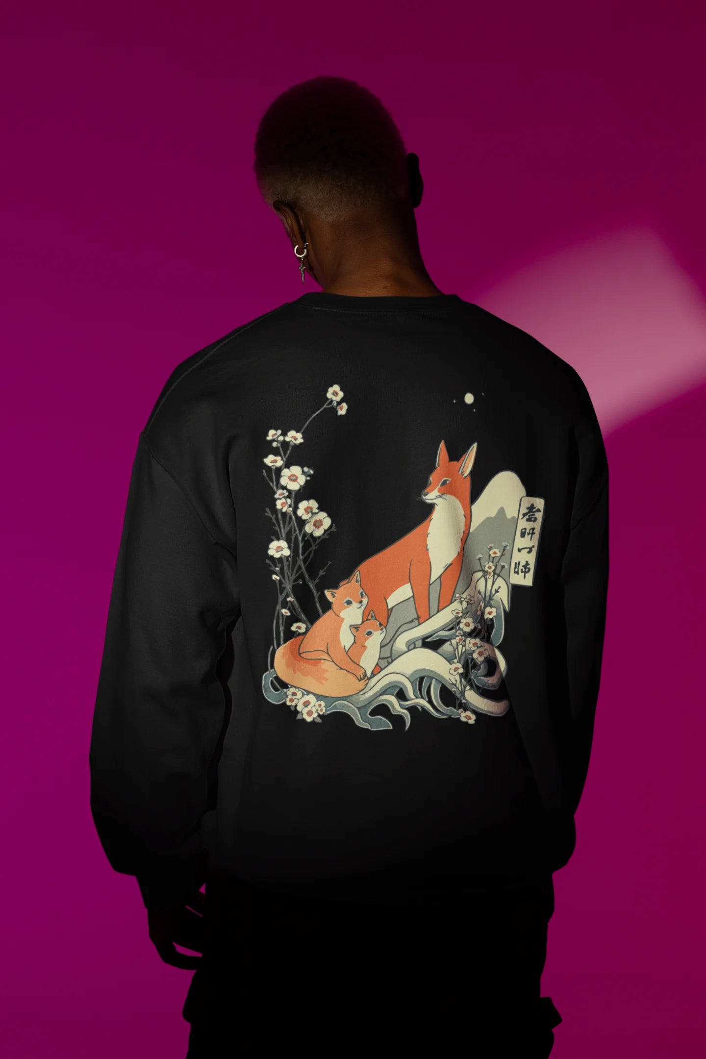 Back view male model wearing a black sweatshirt with a design of a fox and its cub in a traditional Japanese landscape.