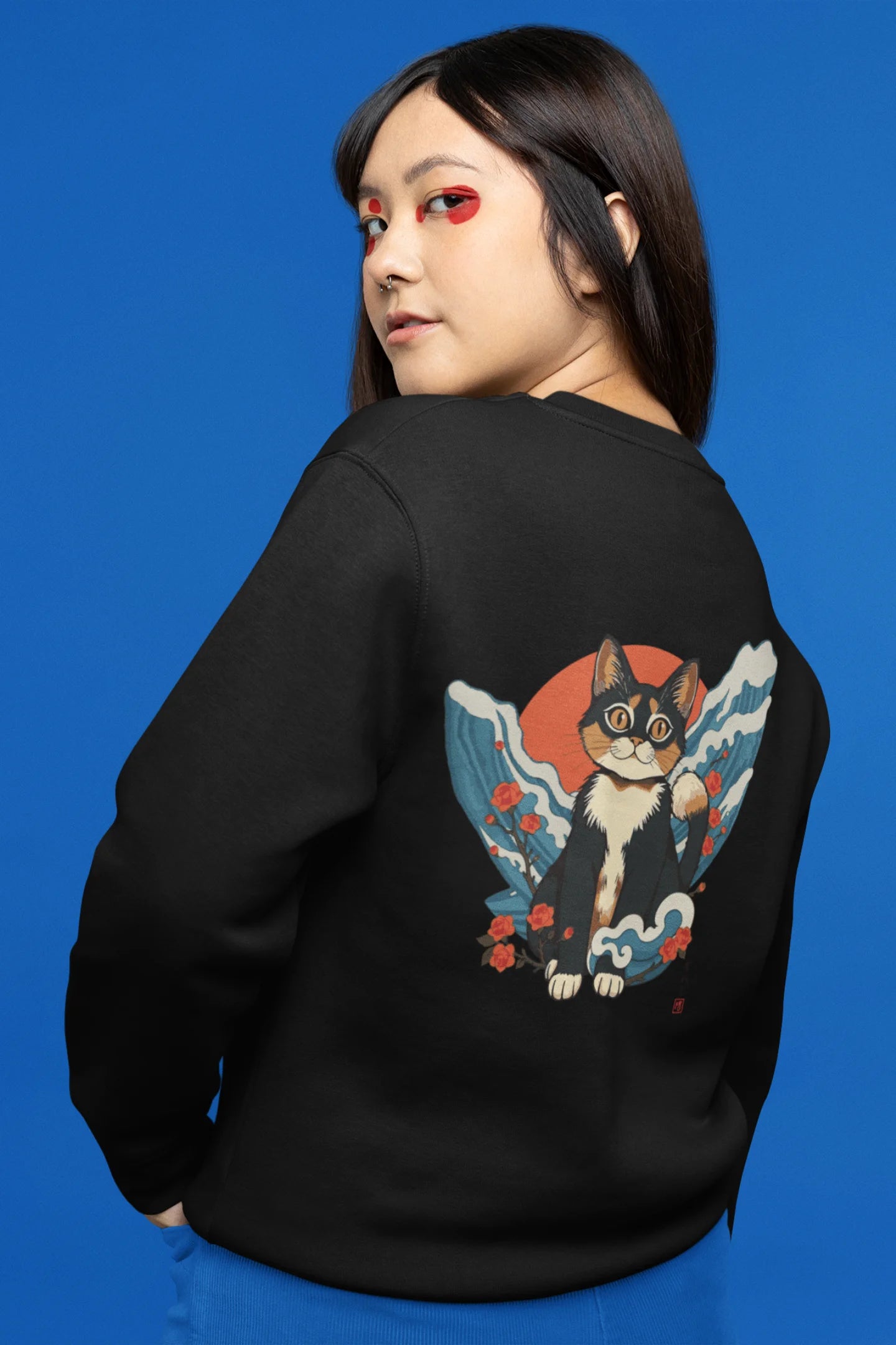 Back view of female model wearing a black sweatshirt with a design of a cat dressed as a samurai, standing against a backdrop of waves and a rising sun.
