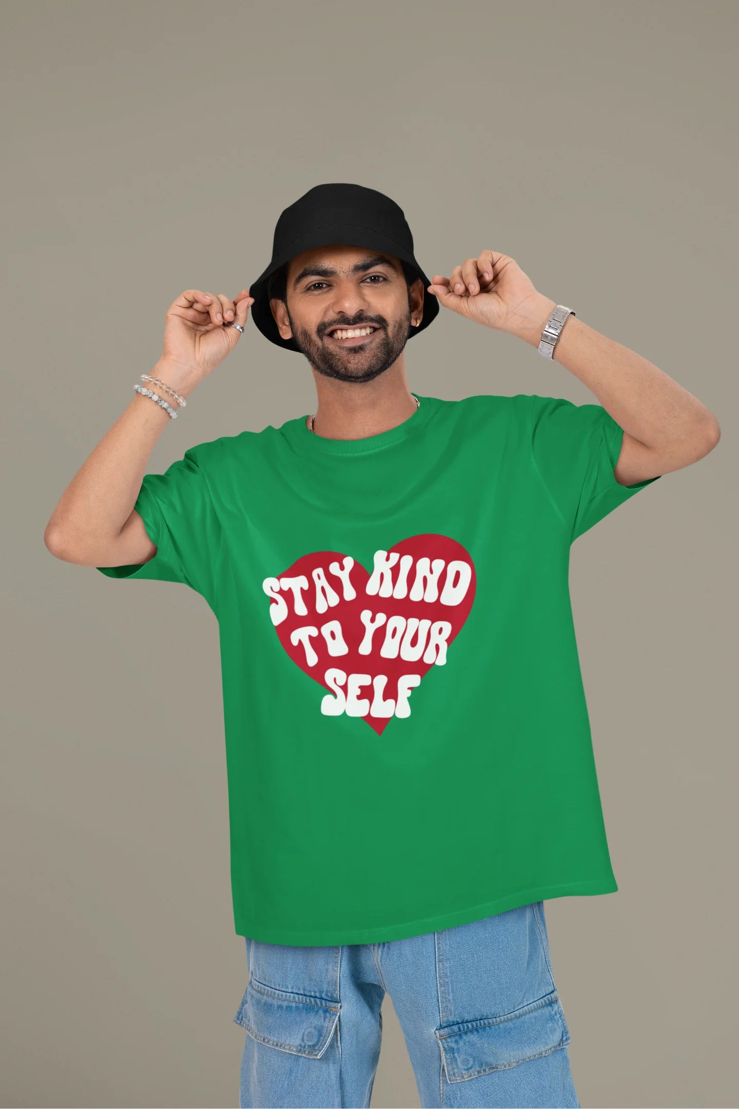 First front view of a male model wearing a forest green oversized t-shirt with the text "Stay Kind" printed on it.