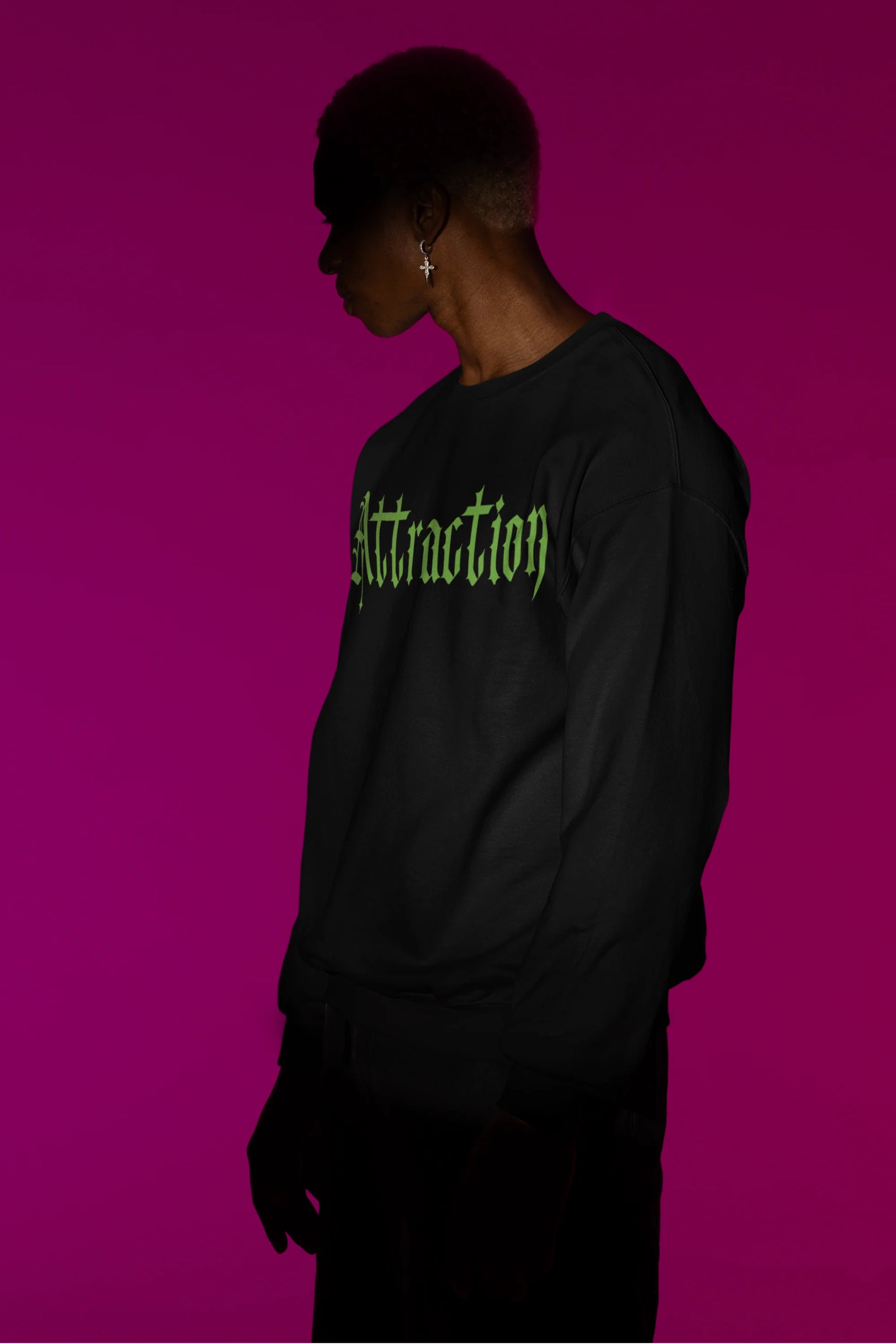 Second front view of a male model wearing a black sweatshirt with a brutalist design featuring two statues kissing and the word "Attraction".