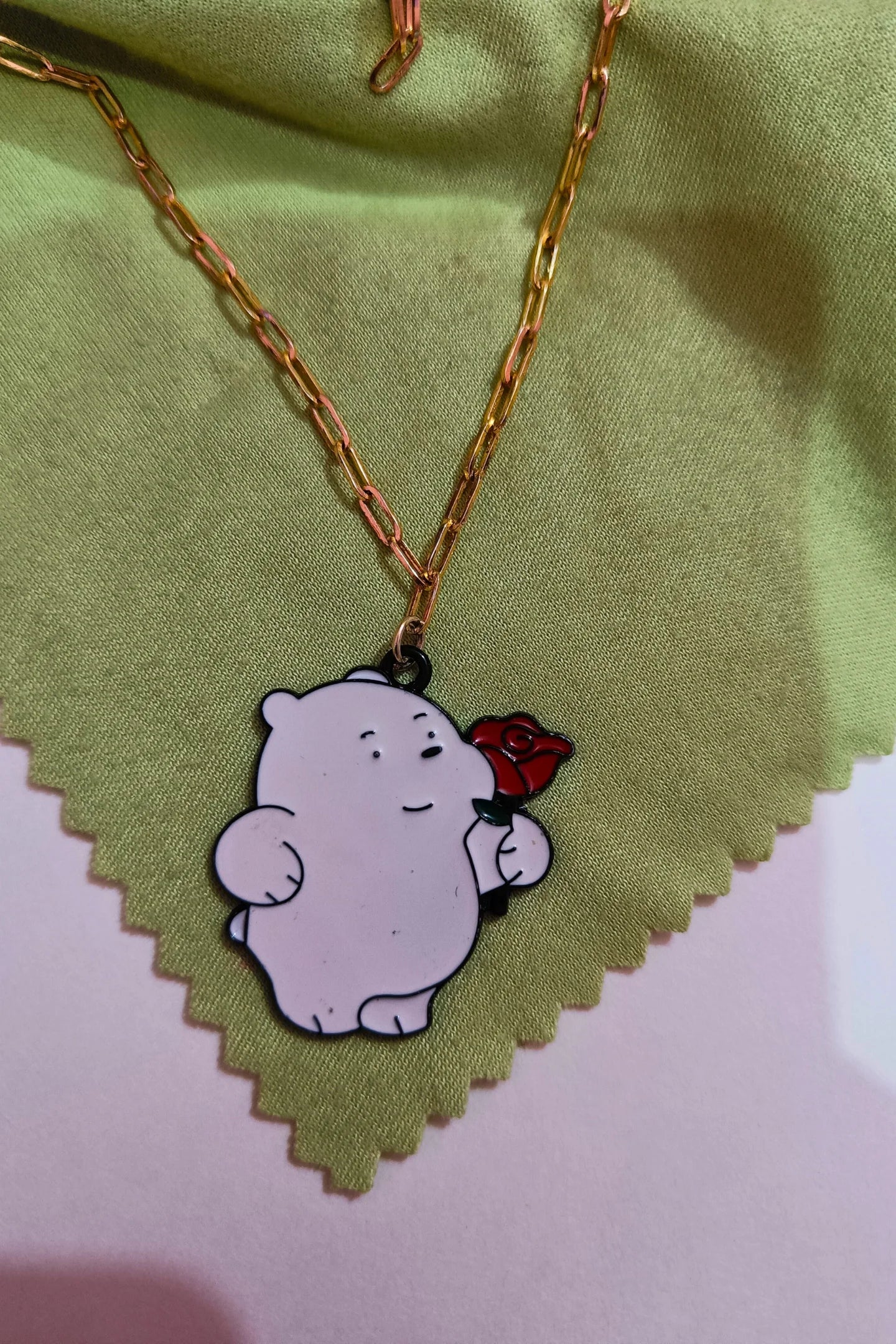 2nd view of a gold chain necklace with a small pendant of Ice Bear from a cartoon, holding a rose.