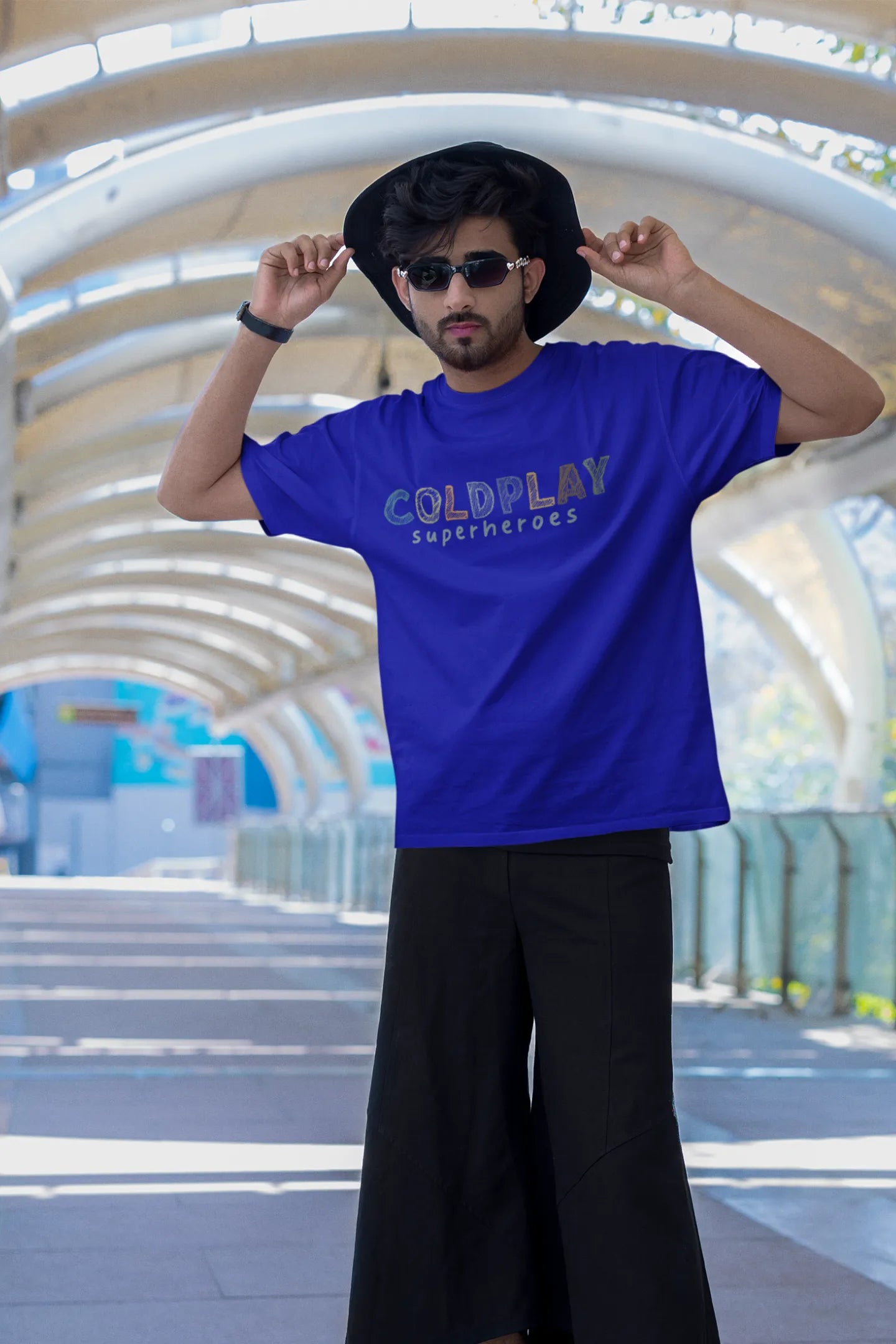 First view of a male model wearing an royal blue oversized t-shirt with a design inspired by the "Something Just Like This" music video, featuring the word "Superheroes".