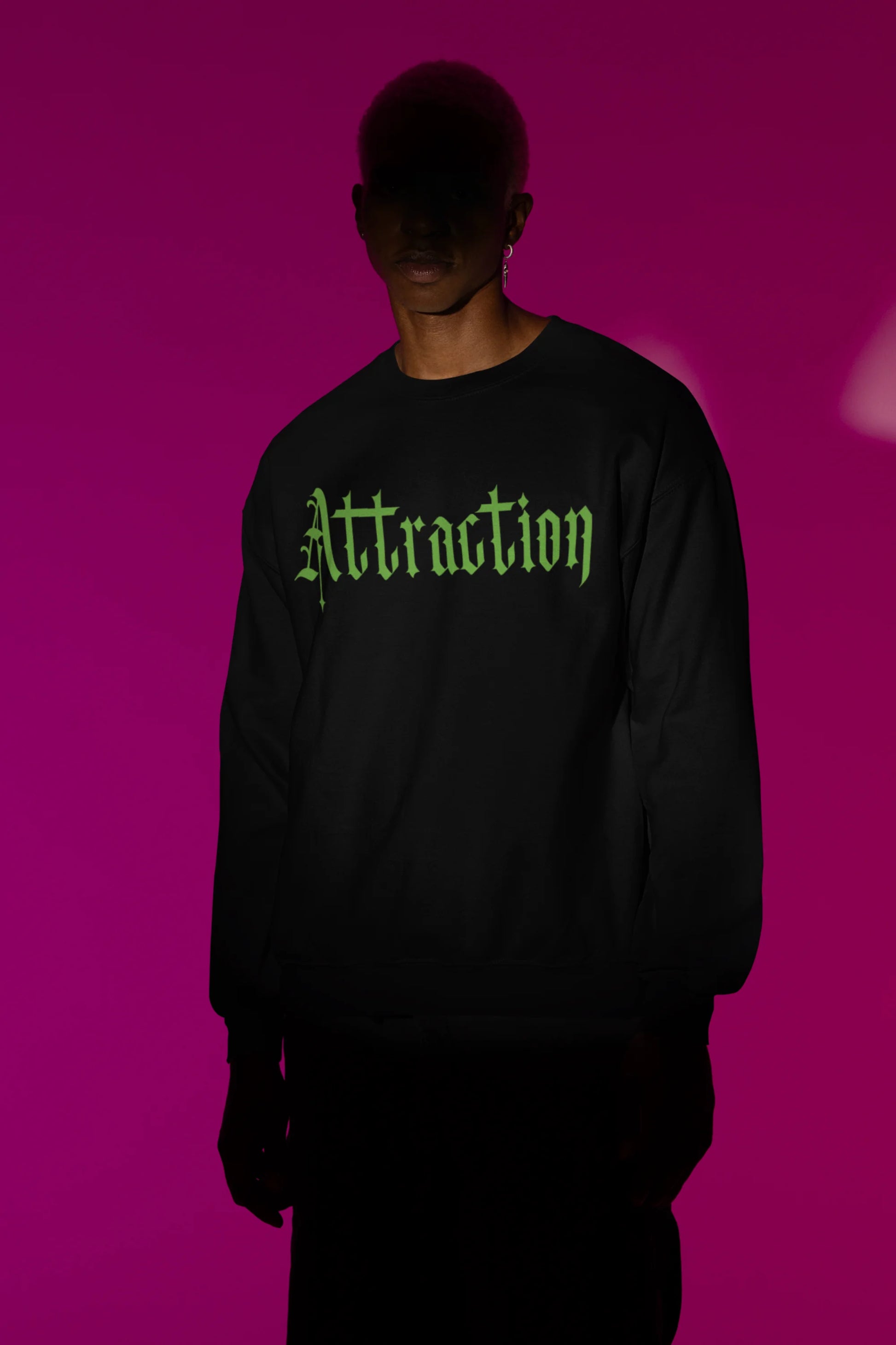 First front view of a male model wearing a black sweatshirt with a brutalist design featuring two statues kissing and the word "Attraction".