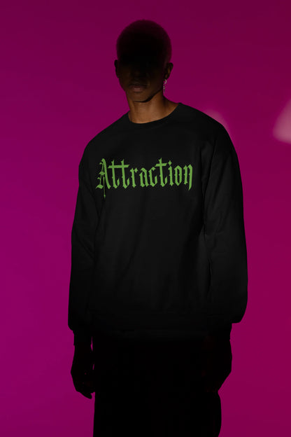 First front view of a male model wearing a black sweatshirt with a brutalist design featuring two statues kissing and the word "Attraction".