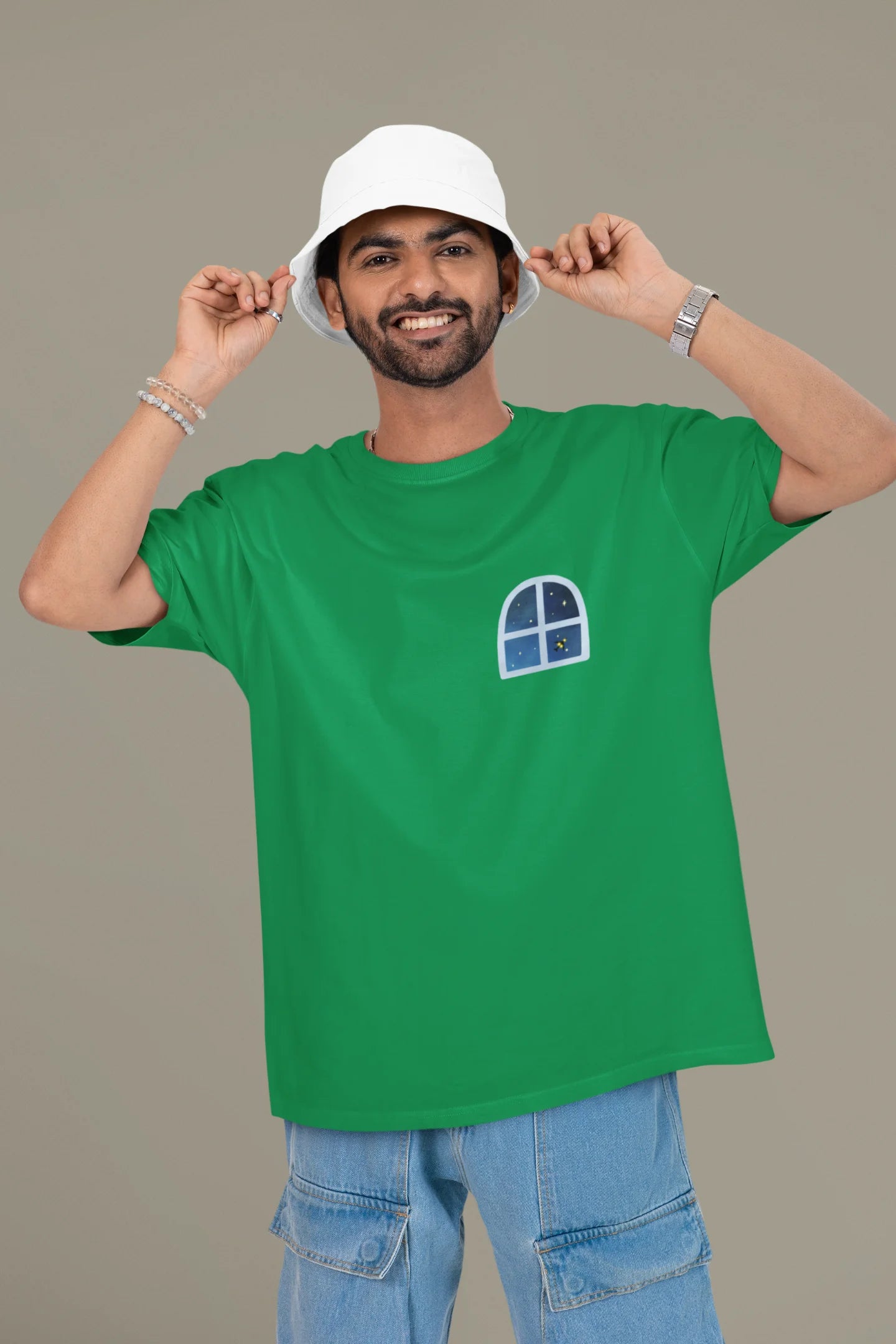 First front view of a male model wearing an forest green oversized t-shirt featuring an illustration called Mithi Neend of children lying or sitting on a rooftop, looking up at a starry night sky.