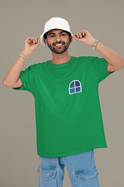 First front view of a male model wearing an forest green oversized t-shirt featuring an illustration called Mithi Neend of children lying or sitting on a rooftop, looking up at a starry night sky.