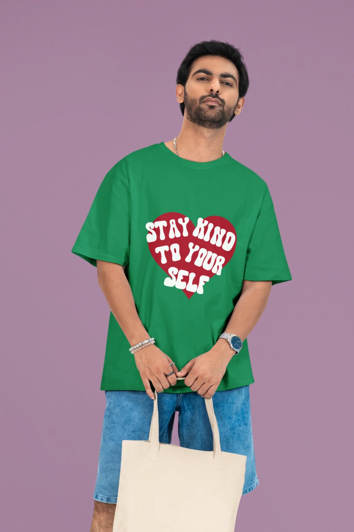 2nd front view of a male model wearing a forest green oversized t-shirt with the text "Stay Kind" printed on it.