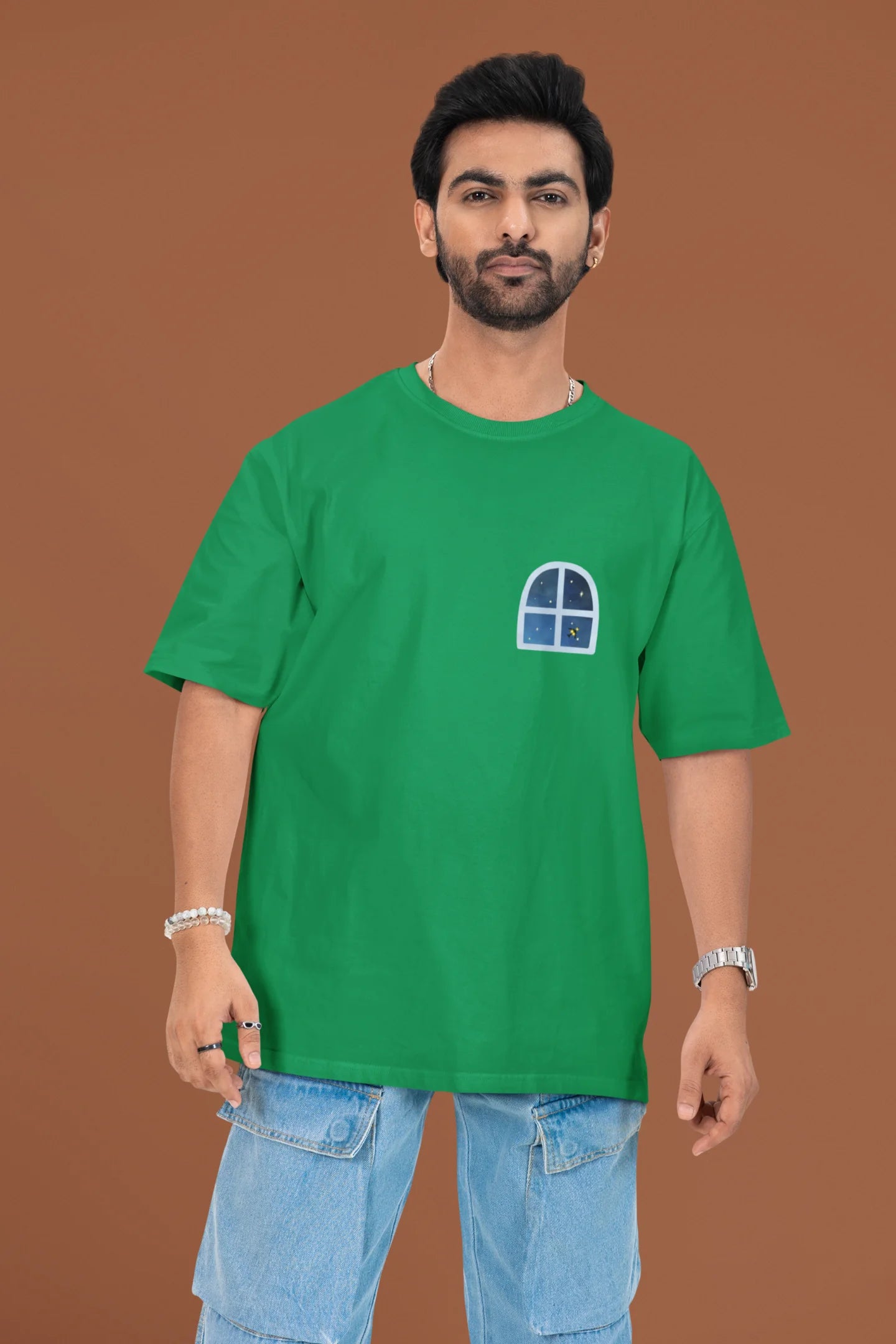 2nd front view of a male model wearing an forest green oversized t-shirt featuring an illustration called Mithi Neend of children lying or sitting on a rooftop, looking up at a starry night sky.