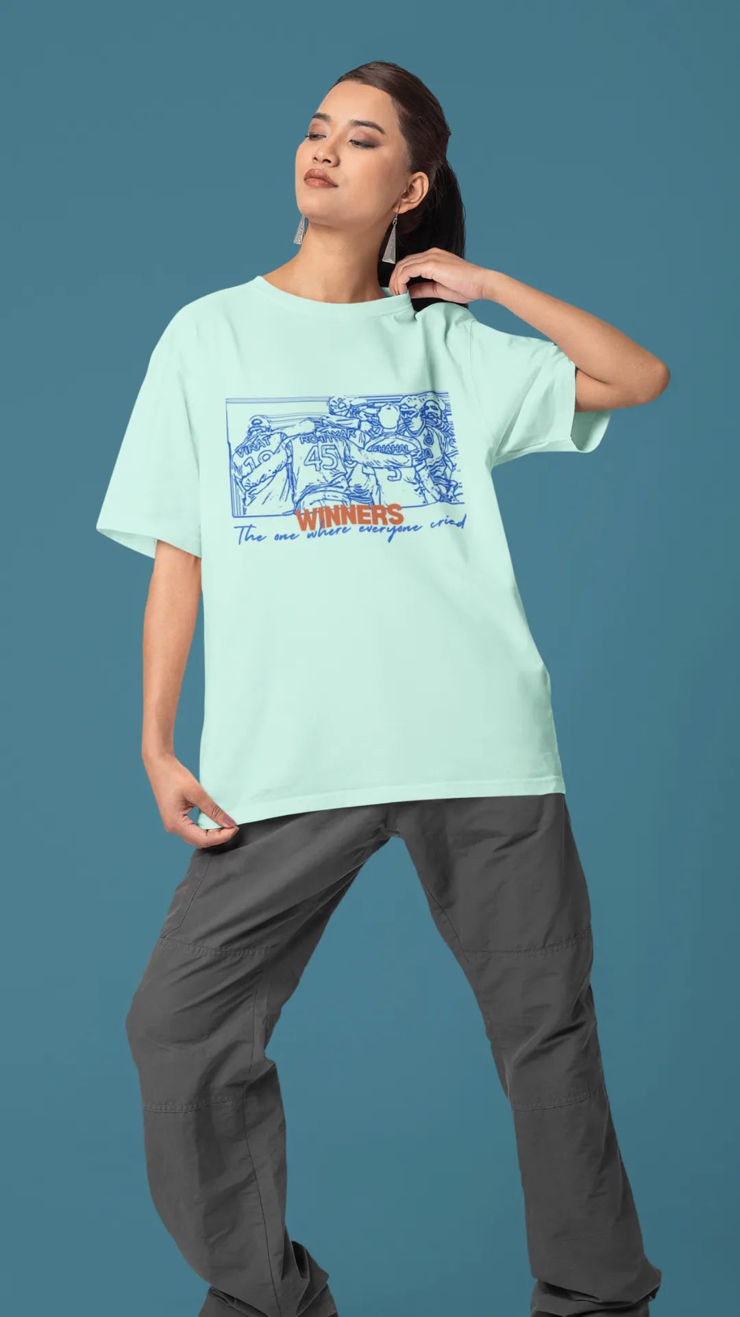 Left side view of a male model wearing an mint-green oversized t-shirt featuring a design of the Indian cricket team in a celebratory huddle with the text "Winners" above them. Ideal for Indian cricket fans commemorating their team's World Cup victory.