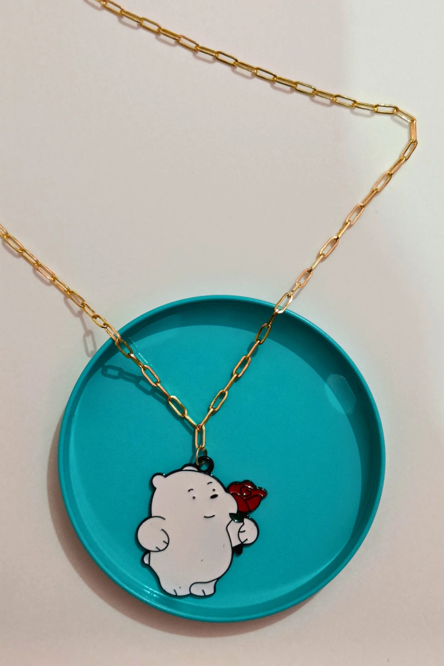 3rd view of a gold chain necklace with a small pendant of Ice Bear from a cartoon, holding a rose.