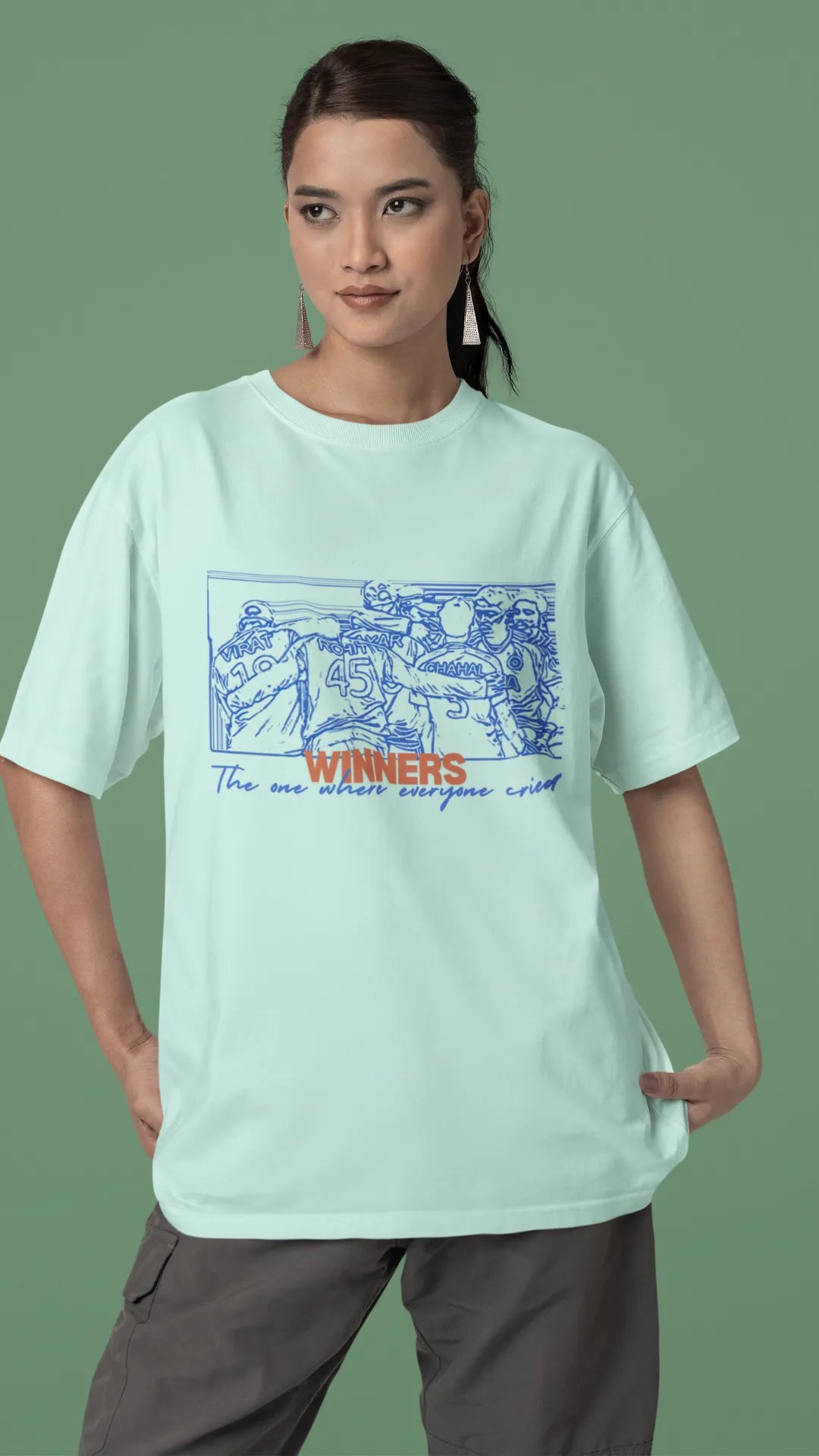 Front view of a female model wearing an mint-green oversized t-shirt featuring a design of the Indian cricket team in a celebratory huddle with the text "Winners" above them. Ideal for Indian cricket fans commemorating their team's World Cup victory.