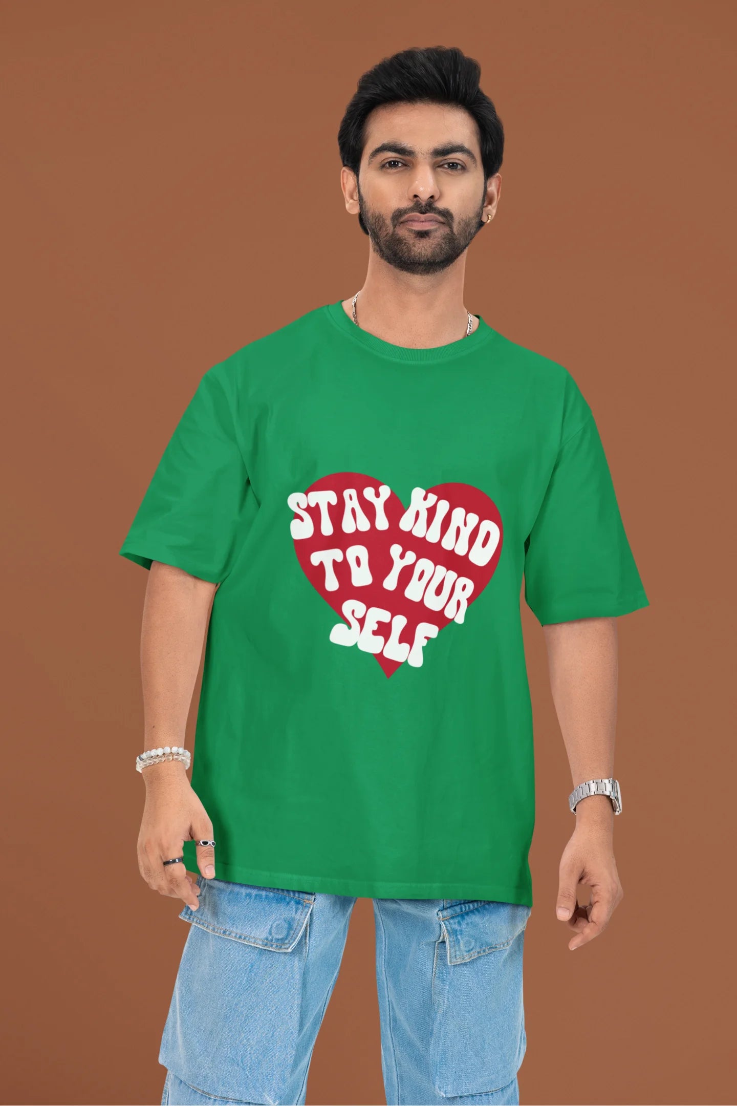 3rd front view of a male model wearing a forest green oversized t-shirt with the text "Stay Kind" printed on it.