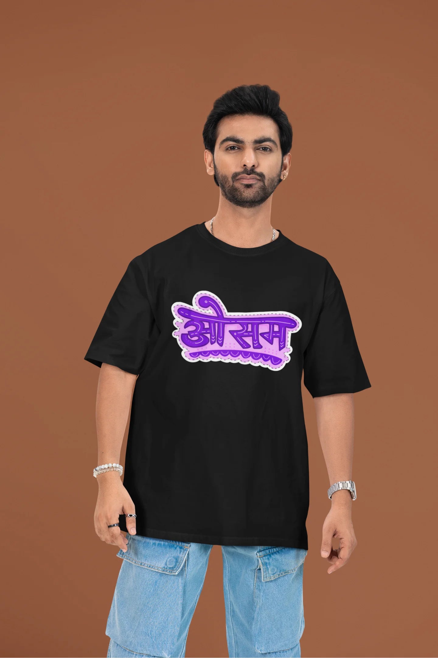 2nd front view of a male model wearing a black colored oversized graphic t-shirt featuring the word "awesome" in a Hindi script.