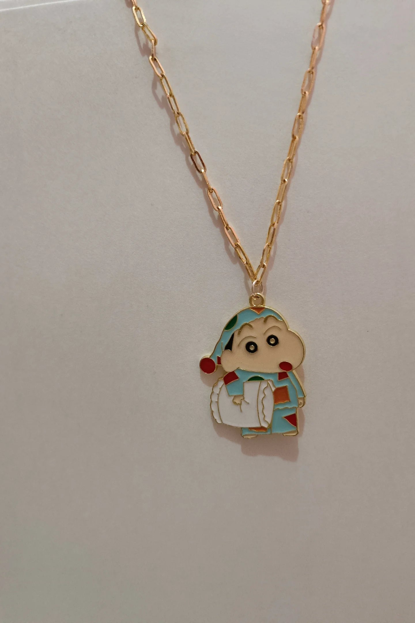 3rd view of a gold chain necklace with a small pendant depicting Shin Chan sleeping.