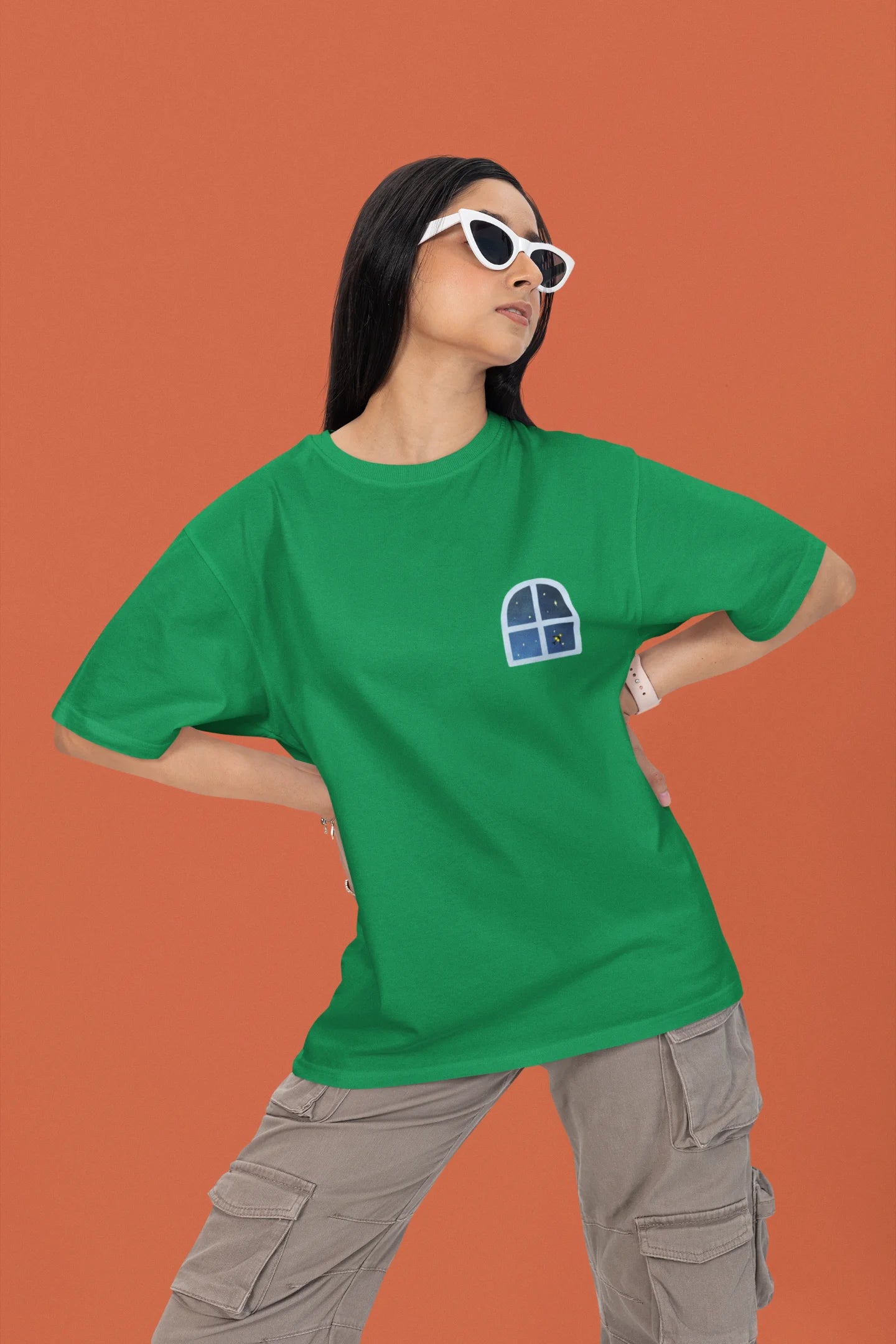 2nd front view of a female model wearing an forest green oversized t-shirt featuring an illustration called Mithi Neend of children lying or sitting on a rooftop, looking up at a starry night sky.