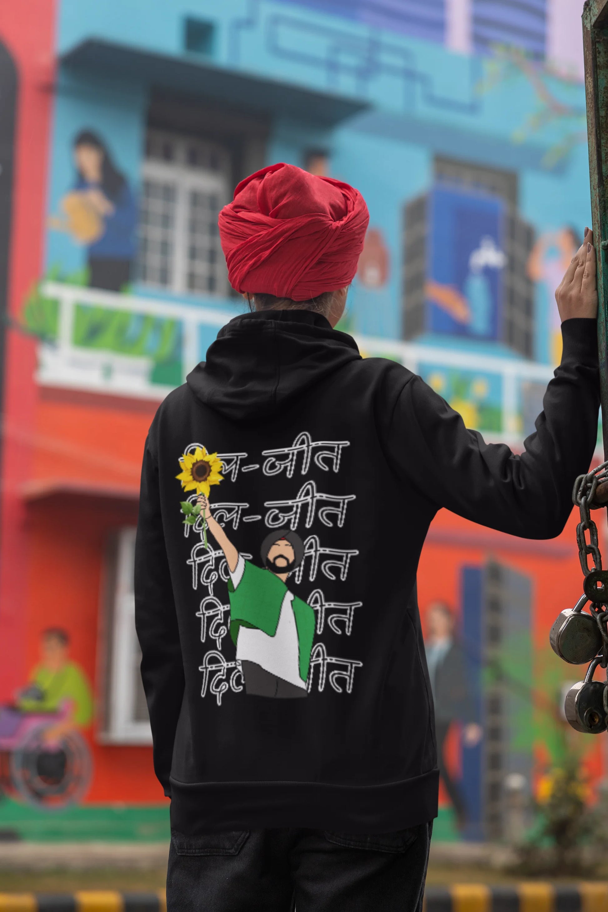 Back view of a female model wearing a black hoodie with Diljit holding up a sunflower with the text "Dil Jeet" in the background.