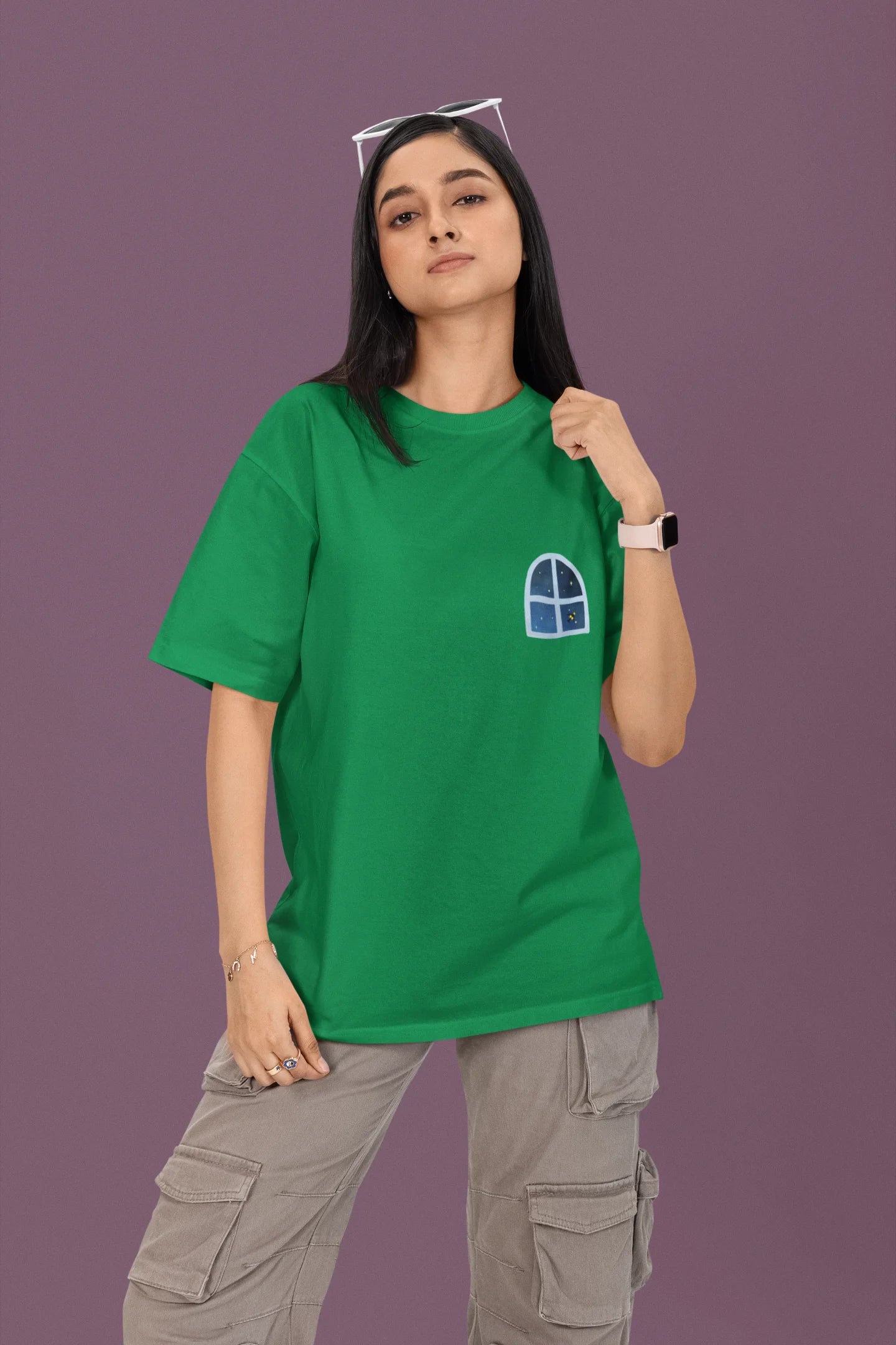 First front view of a female model wearing an forest green oversized t-shirt featuring an illustration called Mithi Neend of children lying or sitting on a rooftop, looking up at a starry night sky.