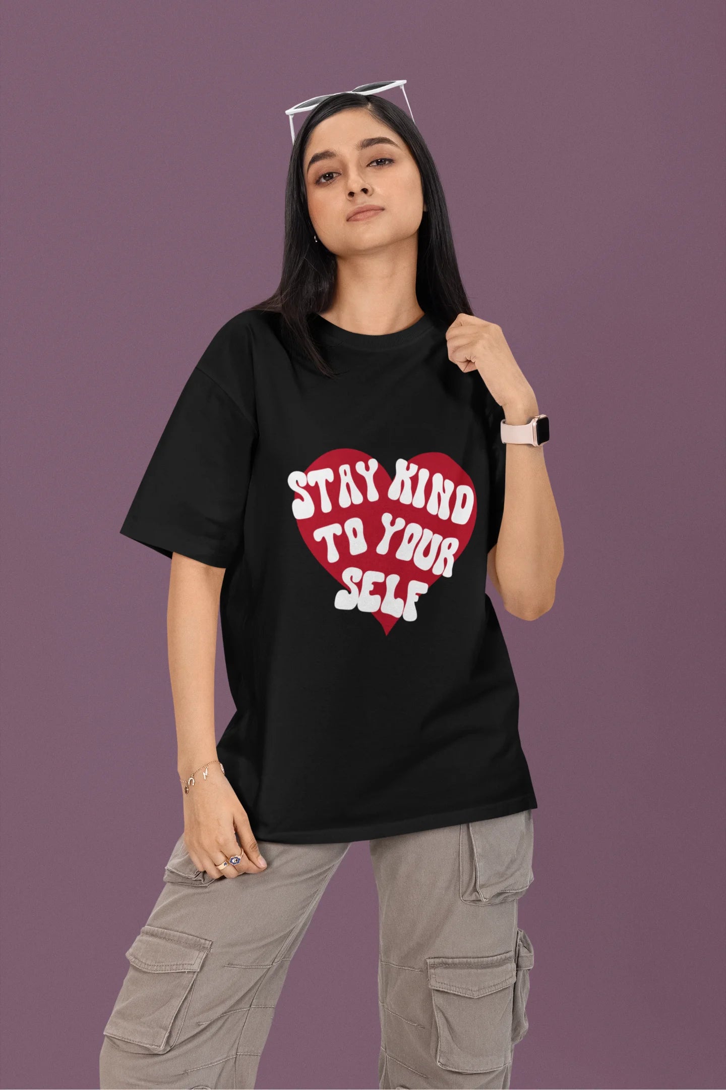 First front view of a female model wearing a black oversized t-shirt with the text "Stay Kind" printed on it.