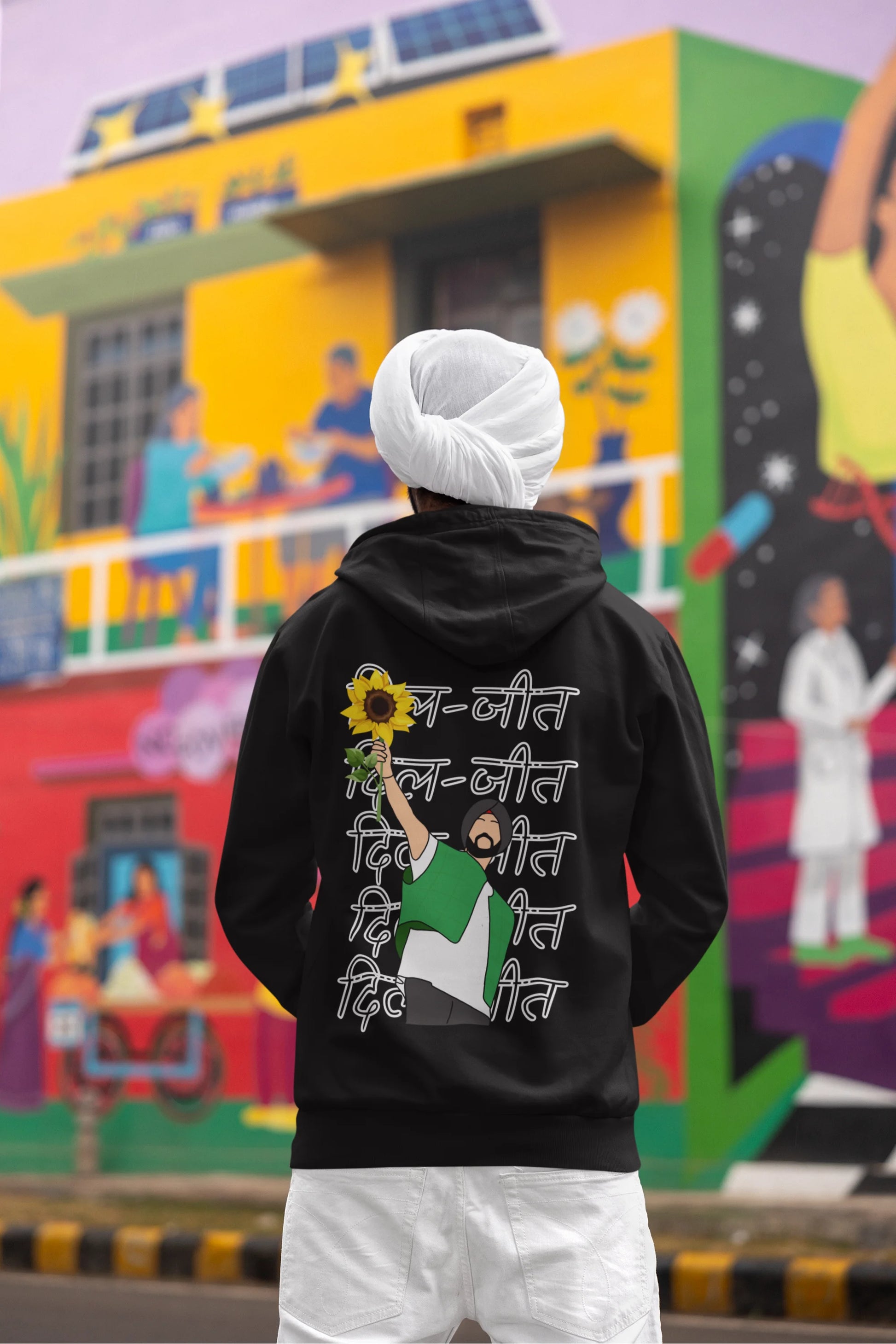 Back view of a male model wearing a black hoodie with Diljit holding up a sunflower with the text "Dil Jeet" in the background.