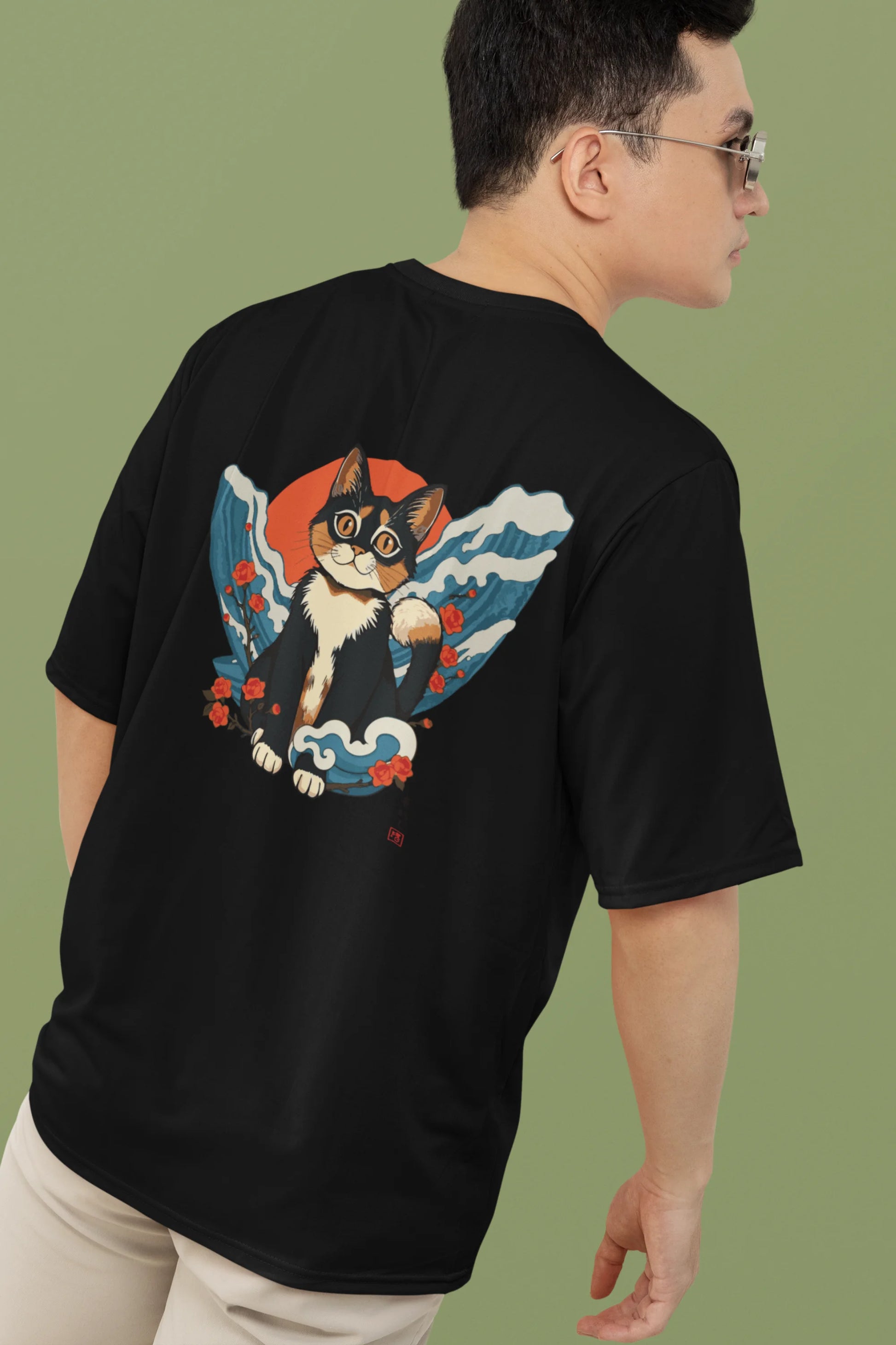 2nd back view of a male model wearing a black oversized tee with a design of a cat dressed as a samurai, standing against a backdrop of waves and a rising sun.