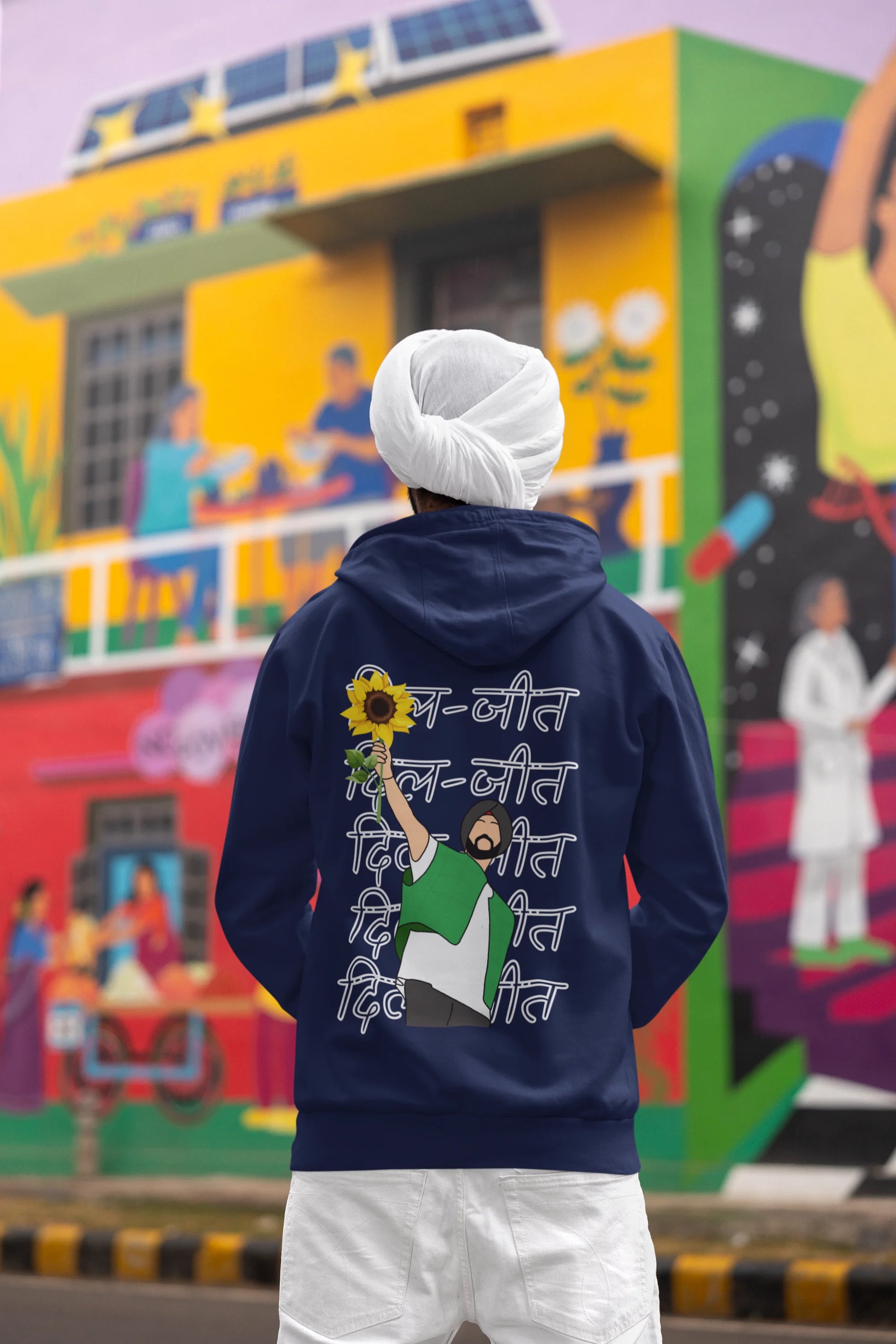 Back view of a male model wearing a royal blue hoodie with Diljit holding up a sunflower with the text "Dil Jeet" in the background.