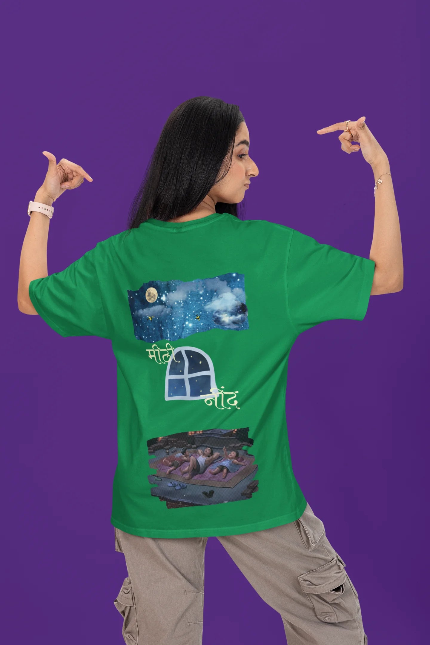 Back view of a female model wearing an forest green oversized t-shirt featuring an illustration called Mithi Neend of children lying or sitting on a rooftop, looking up at a starry night sky.