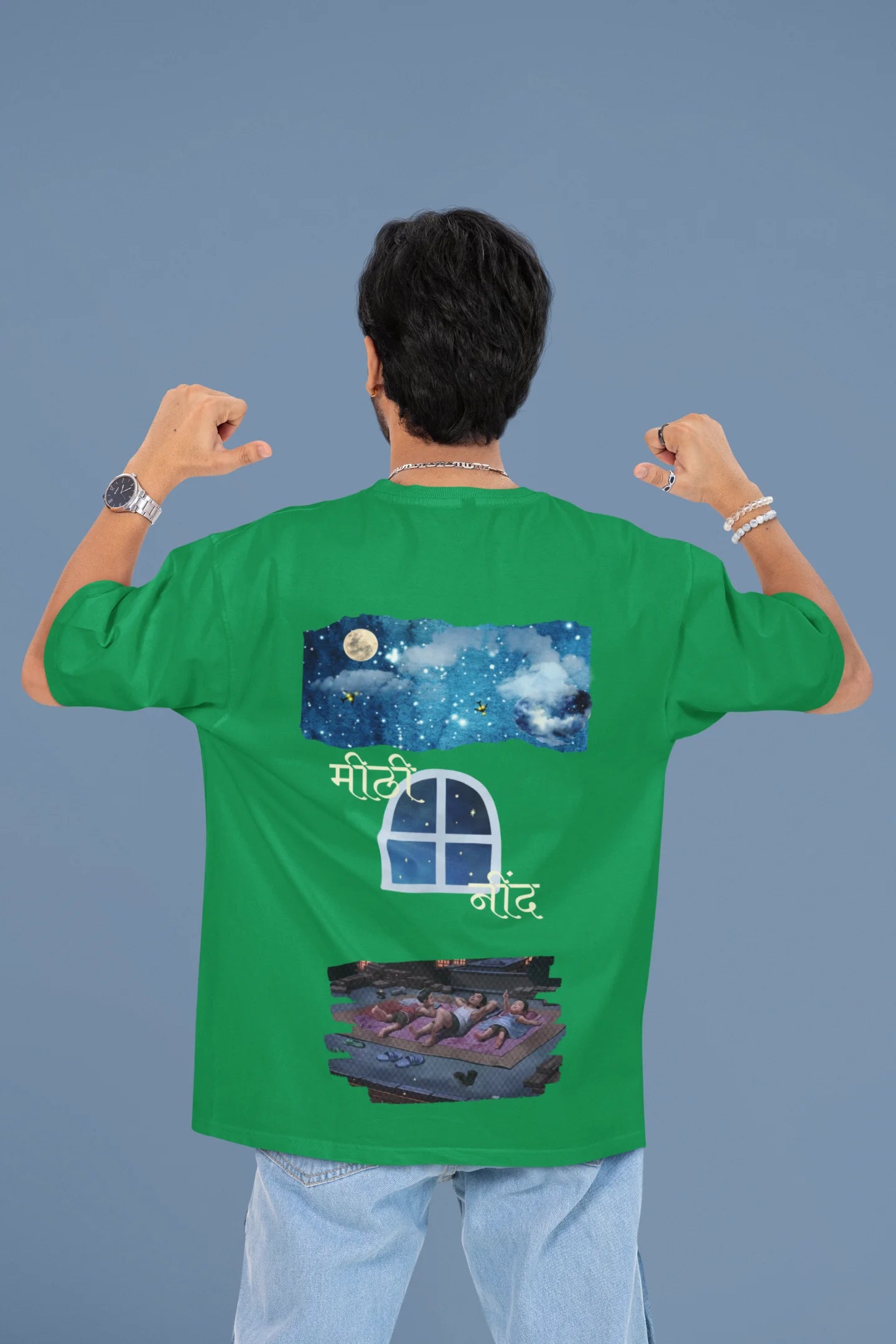 Back view of a male model wearing an forest green oversized t-shirt featuring an illustration called Mithi Neend of children lying or sitting on a rooftop, looking up at a starry night sky.