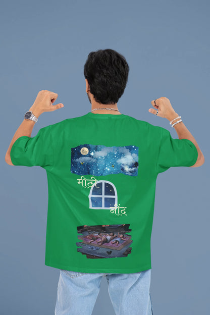 Back view of a male model wearing an forest green oversized t-shirt featuring an illustration called Mithi Neend of children lying or sitting on a rooftop, looking up at a starry night sky.