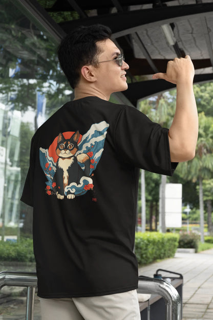 First back view of a male model wearing a black oversized tee with a design of a cat dressed as a samurai, standing against a backdrop of waves and a rising sun.