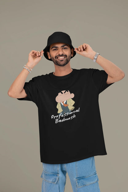 First front view of a male model wearing a black oversized t-shirt featuring Shinchan wearing a suit and trench coat with text saying "Professional Badmosh".