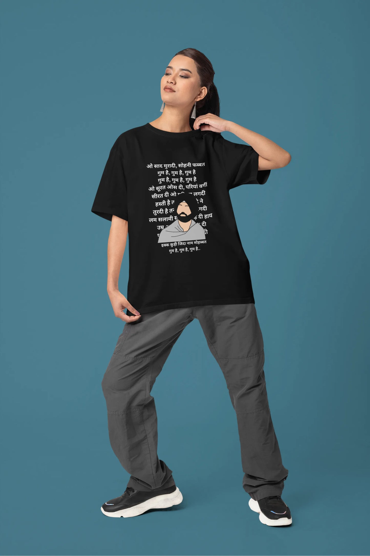 Fourth front view of a female model wearing a black oversized  T-shirt with a Diljit Dosanjh portrait  with lyrics from the song "Ikk Kudi" in the background.
