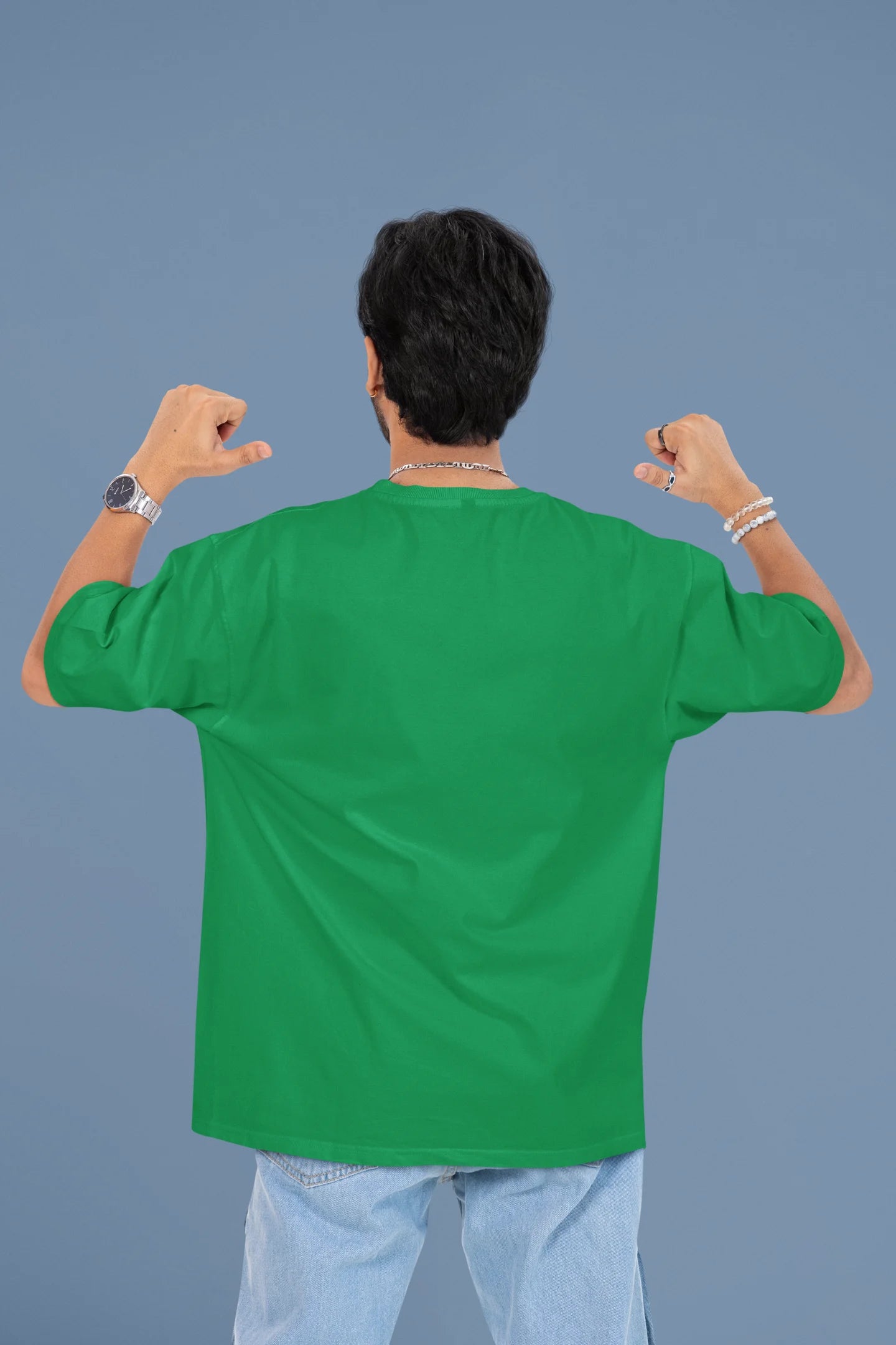 Back view of a male model wearing a forest green oversized t-shirt with the text "Stay Kind" printed on it.