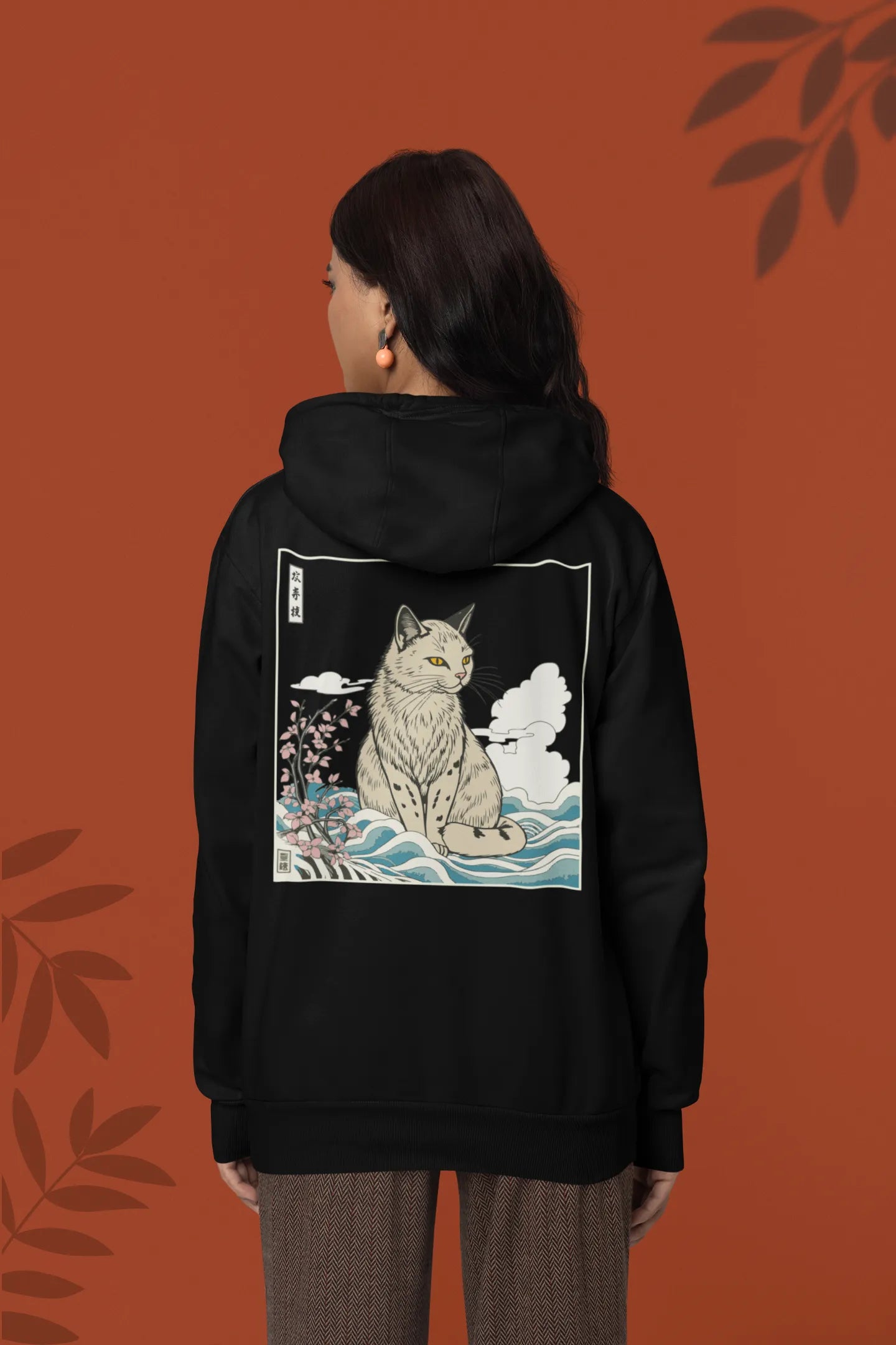 Back view of a female model wearing a black hoodie with a design of a wildcat sitting on ocean waves.