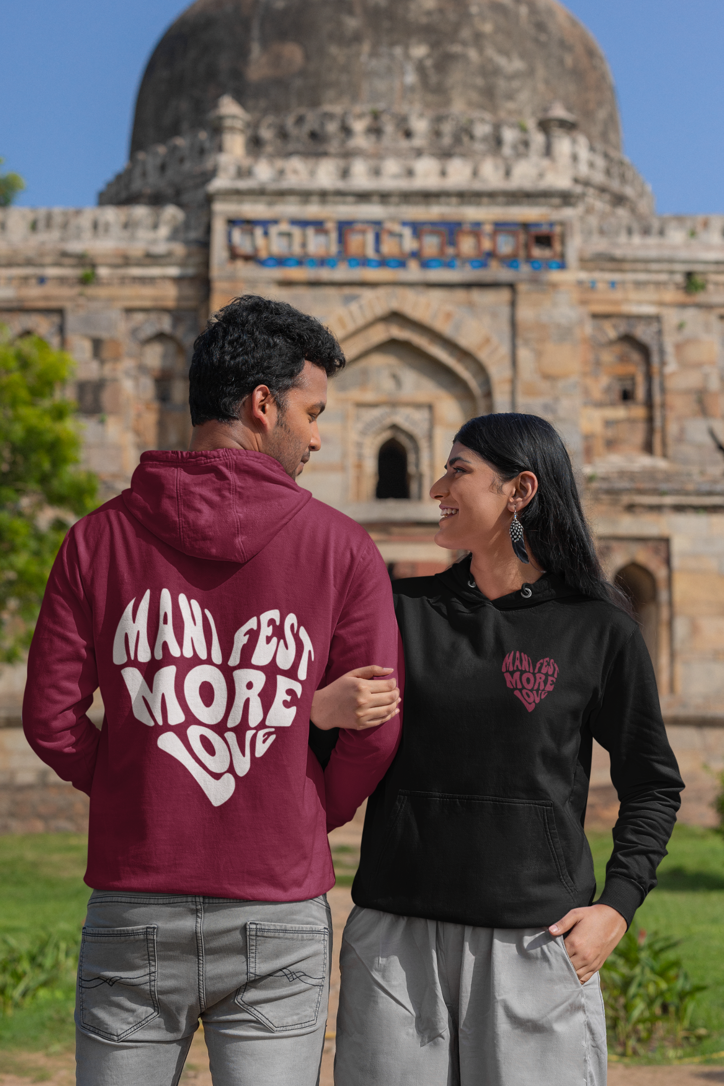 2nd front and back view of a couple wearing matching hoodies, each with a heart design containing the words "Manifest More Love."