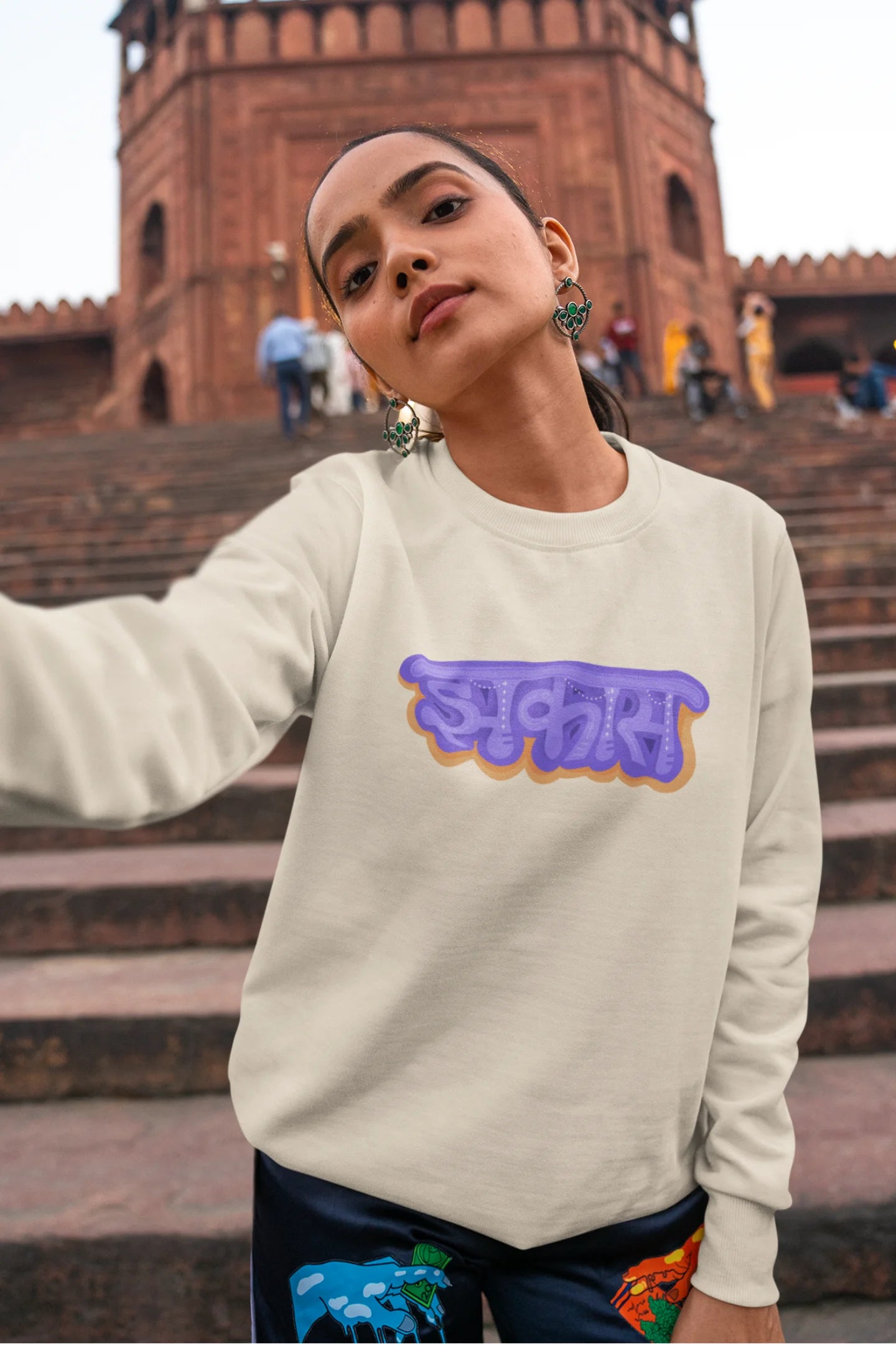 4th front view of a female model wearing an cream sweatshirt featuring "Jhakas" in a stylish font.